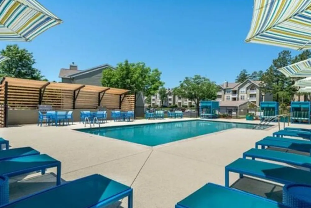Luxurious apartment pool area with inviting blue lounge chairs, vibrant striped umbrellas, and serene landscaping perfect for relaxation.