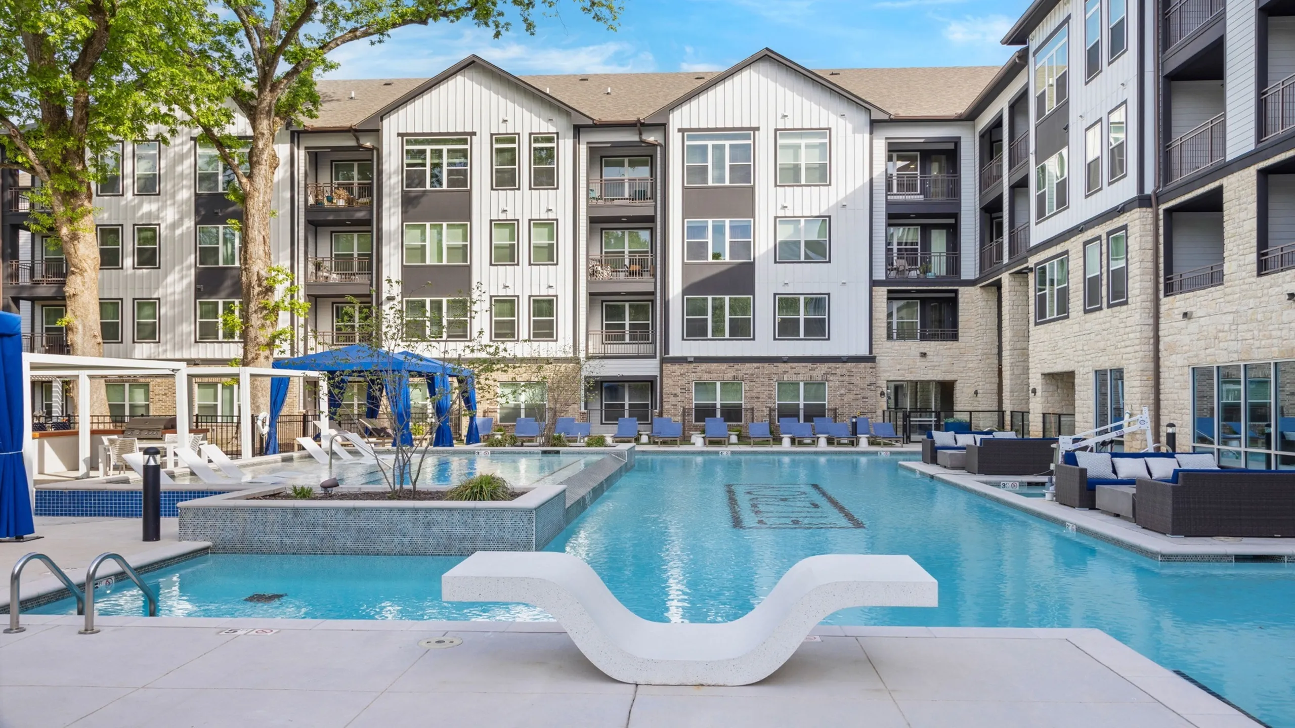 Luxurious apartment complex featuring a sparkling swimming pool, elegant cabanas, and modern lounge areas surrounded by lush greenery.