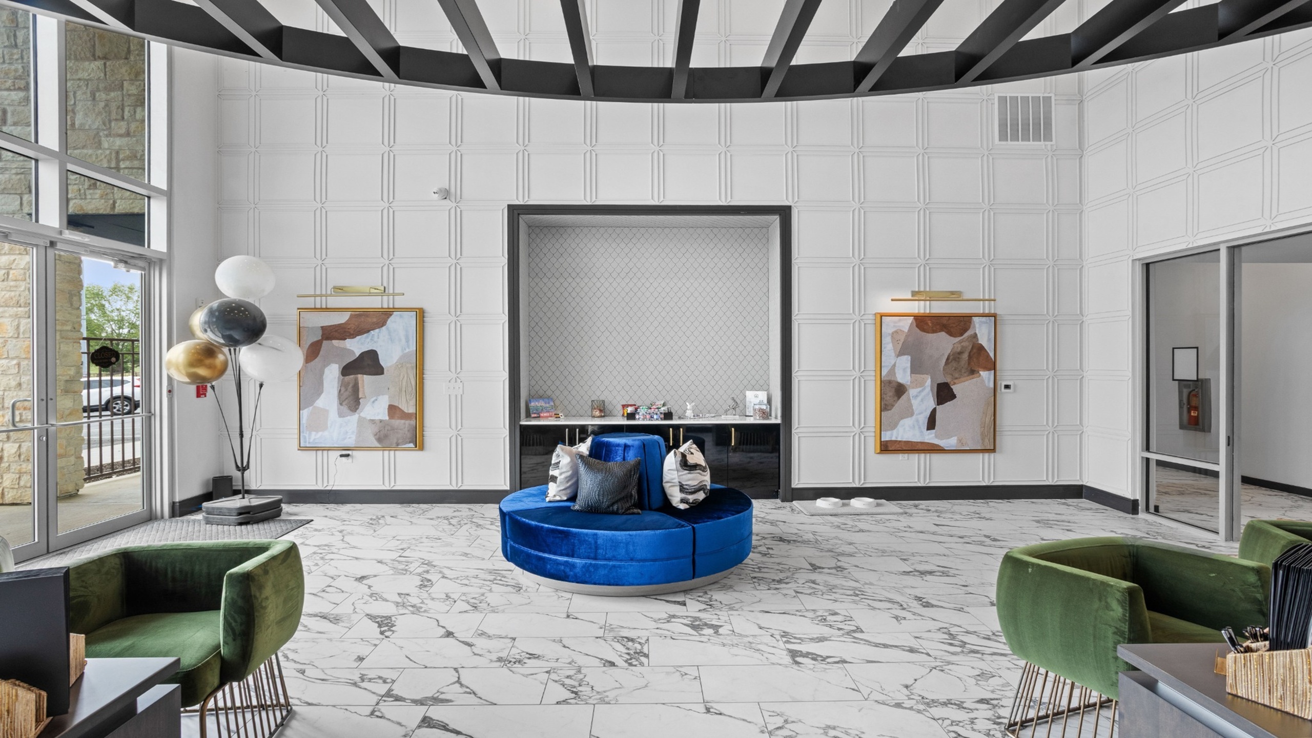 Elegant apartment lobby showcasing a modern interior with marble flooring, plush blue seating, and stylish abstract artwork, complemented by natural light through large windows.