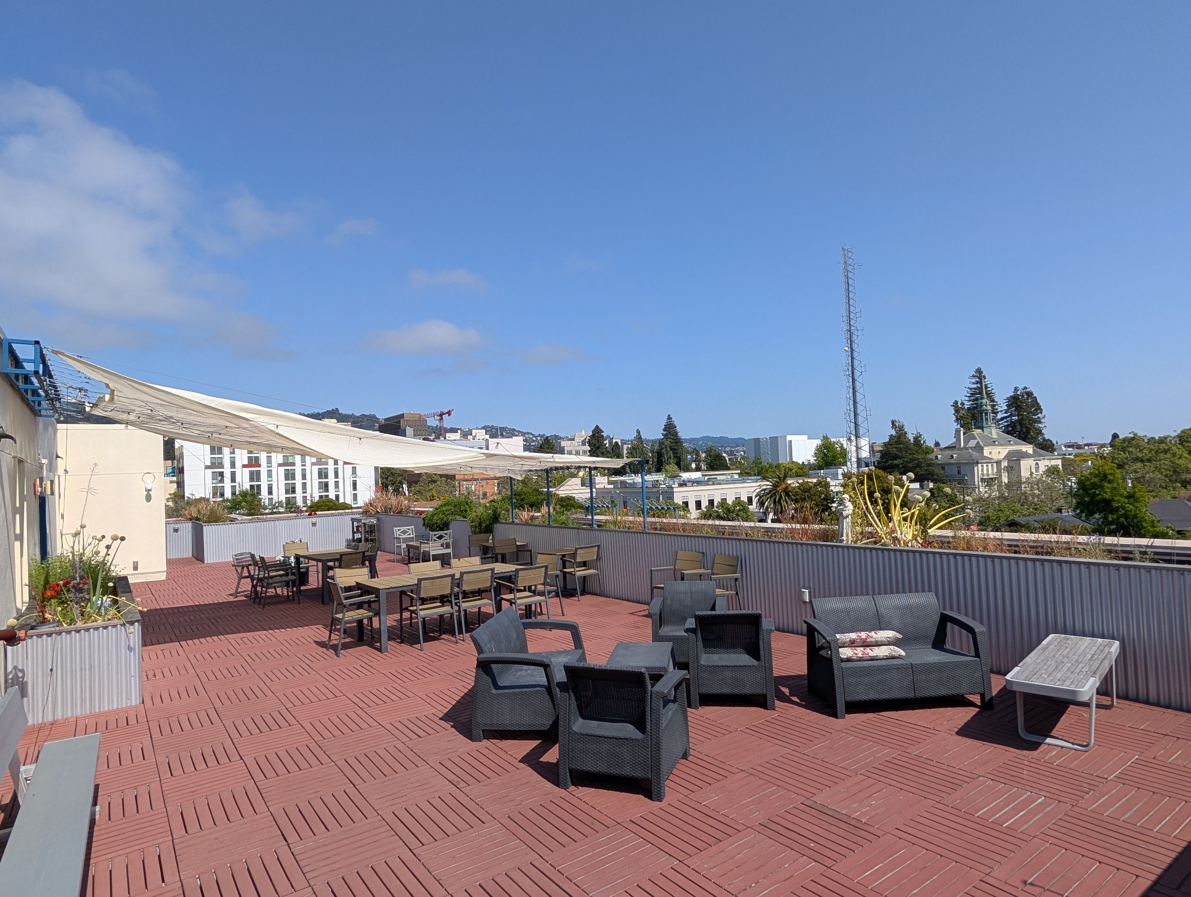 Charming rooftop terrace with modern outdoor seating, lush greenery, and stunning panoramic city views under a clear blue sky.