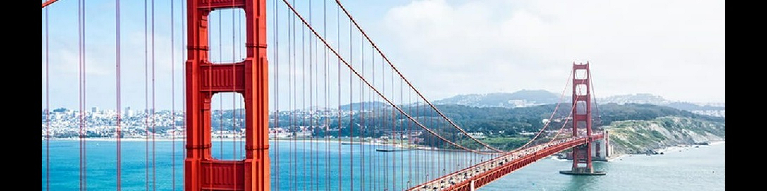 Iconic red suspension bridge spanning a vibrant blue bay with rolling hills in the background, showcasing architectural beauty and stunning natural scenery.