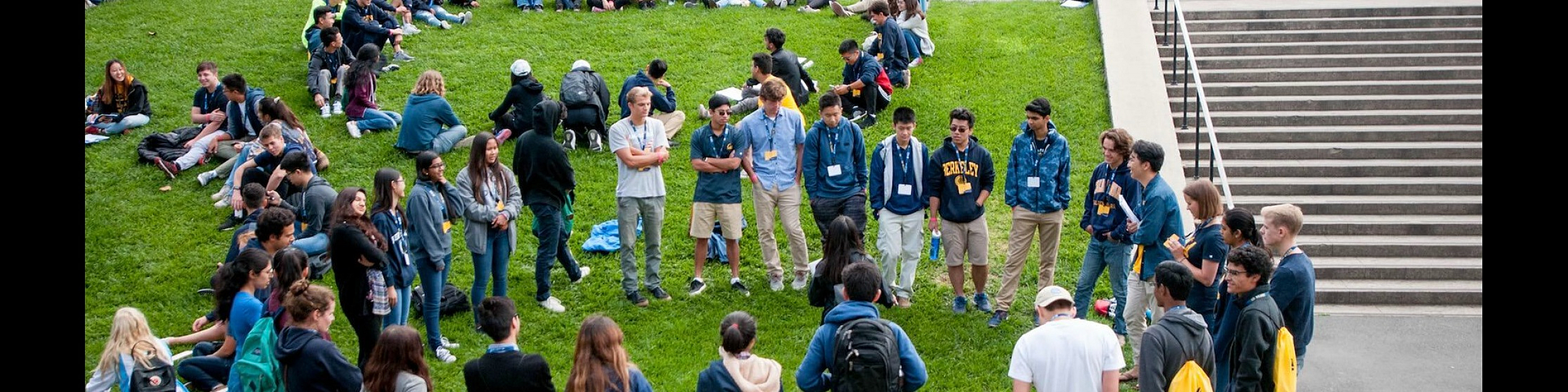 Vibrant campus scene with students gathering on a lush green lawn, surrounded by beautiful architecture and blooming flowers.