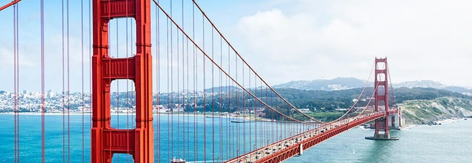 Iconic red suspension bridge gracefully spanning across a stunning blue bay, surrounded by lush green hills and a vibrant cityscape.