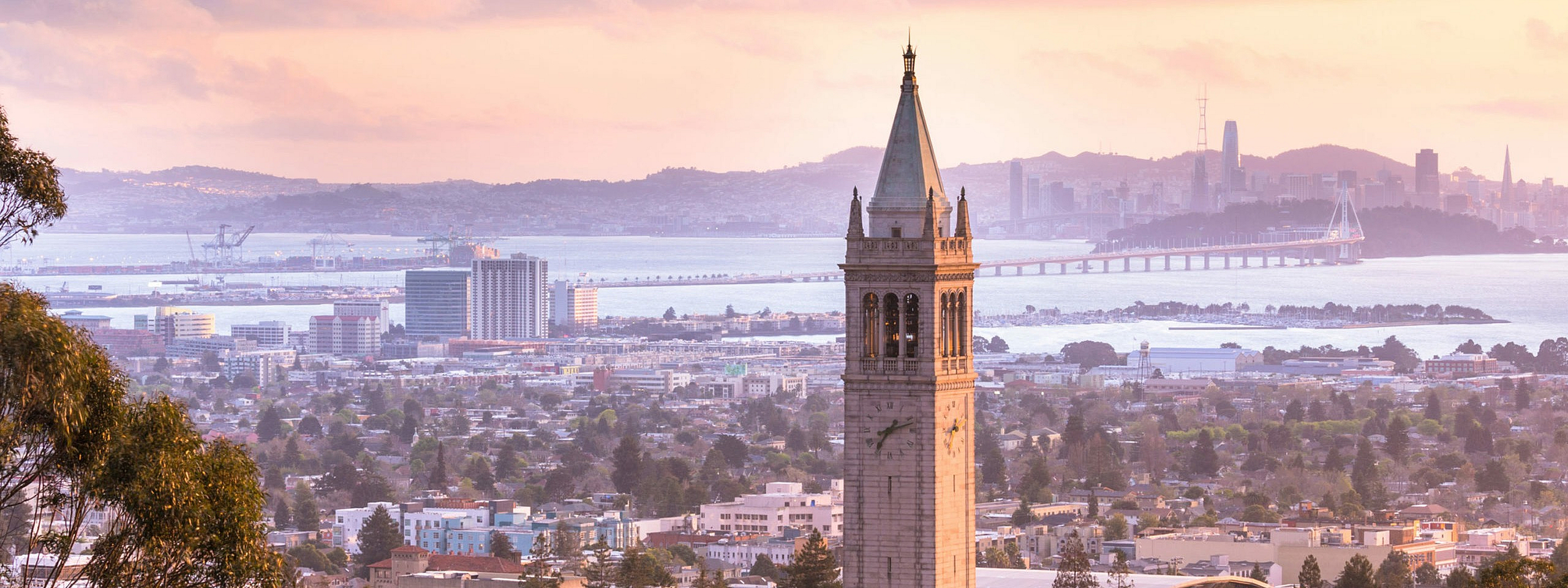 Captivating view of a historic bell tower with a sprawling cityscape and scenic bay backdrop at sunset.