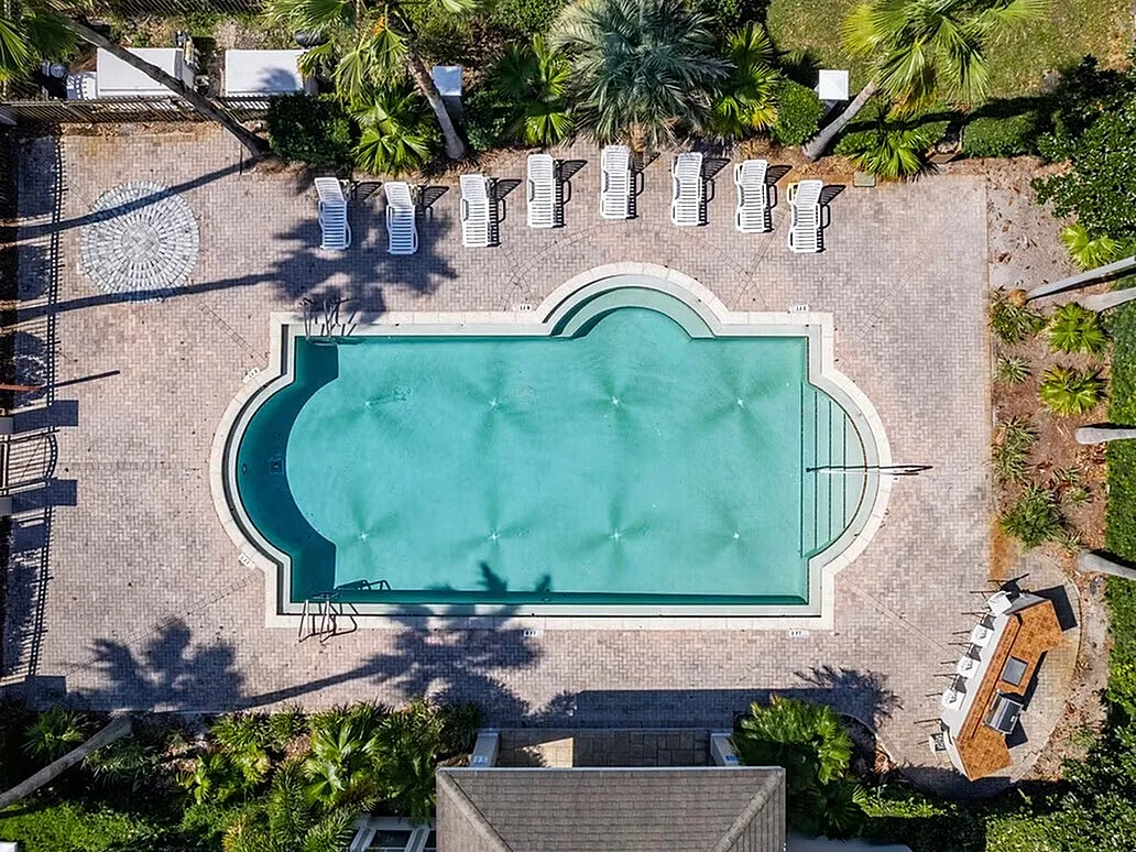 Stunning aerial view of a luxurious swimming pool surrounded by lush palm trees and chic lounging chairs, offering a perfect relaxation oasis.