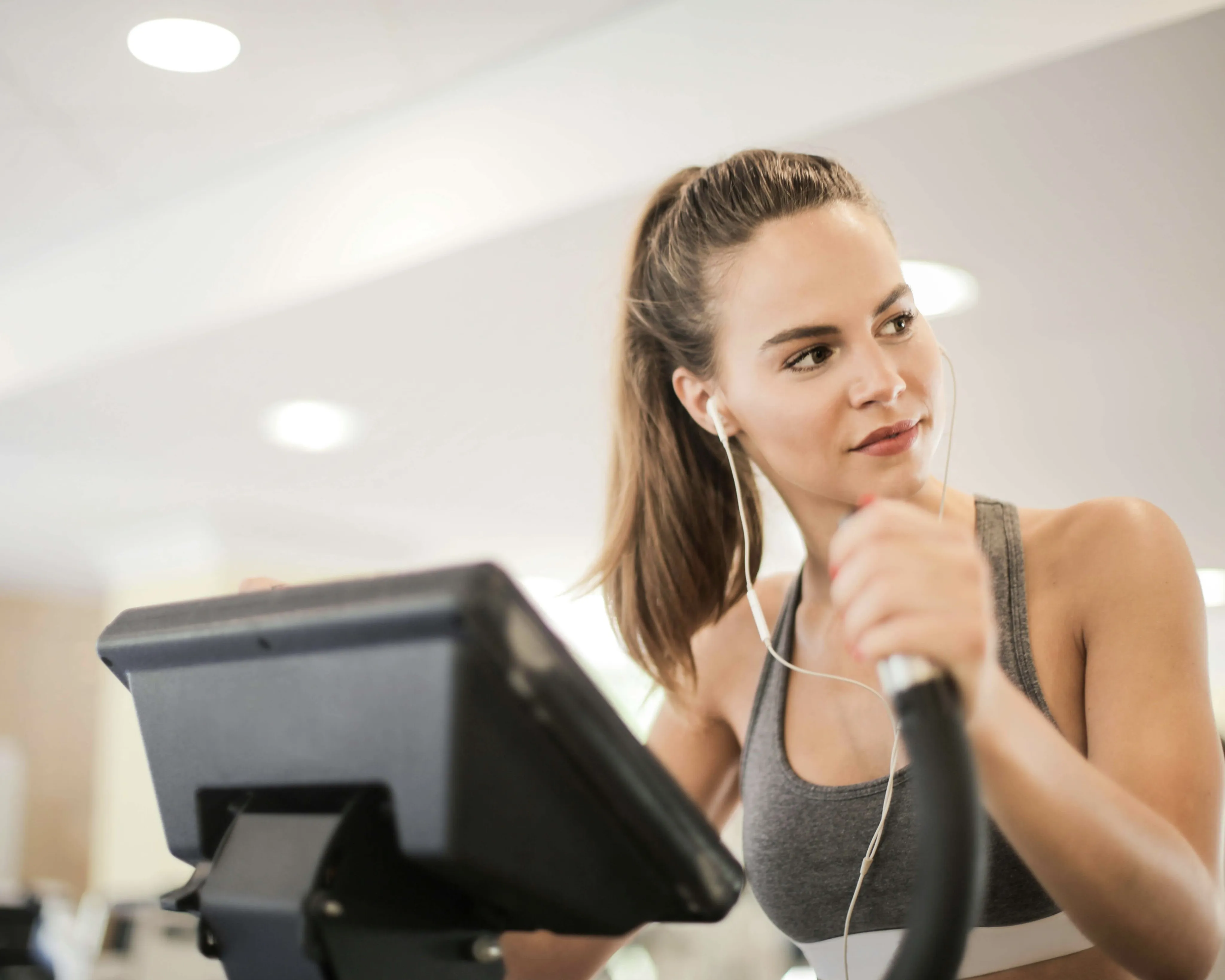 Energetic woman enjoying a workout on an exercise machine, wearing headphones in a modern fitness center.