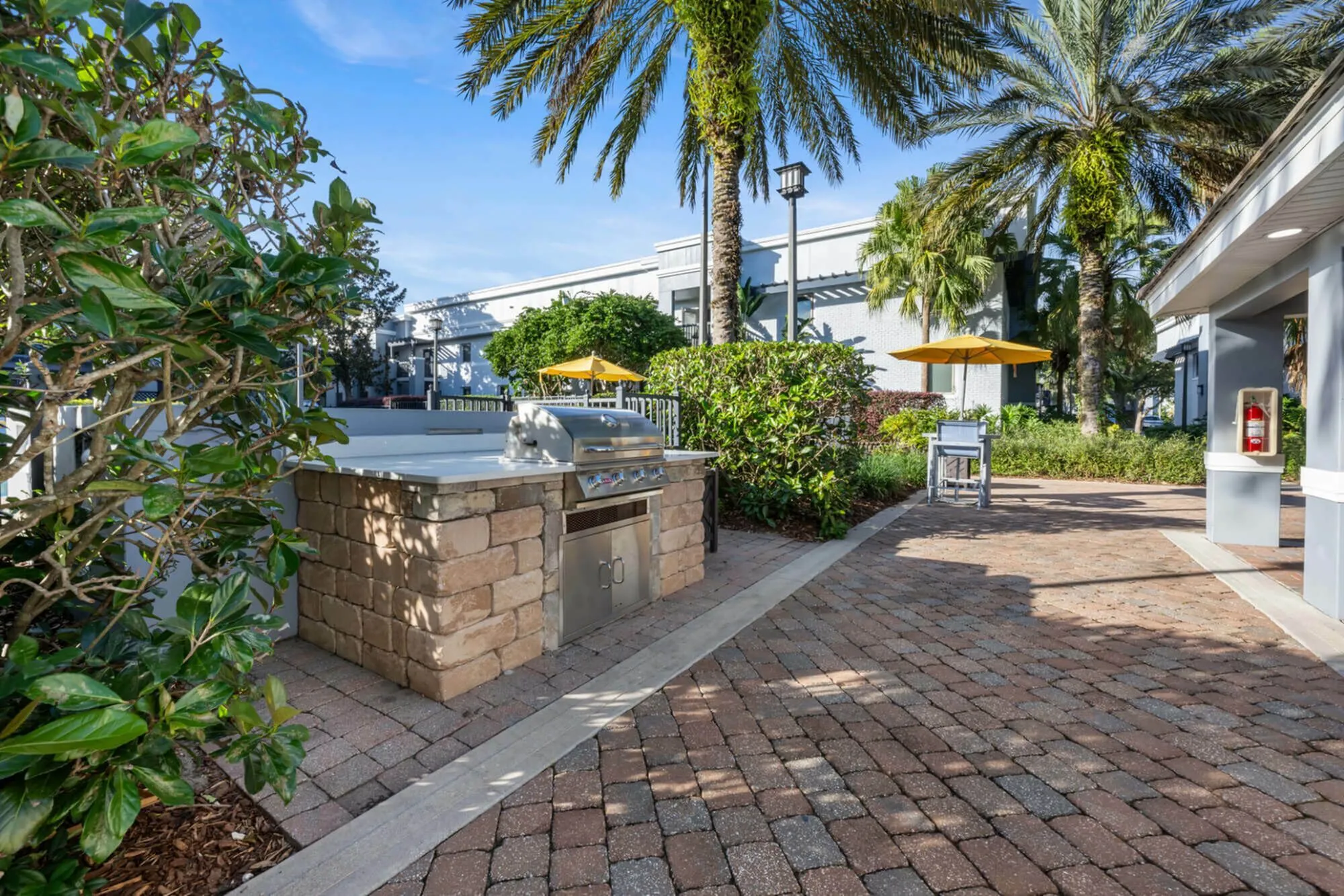 Inviting outdoor patio area with a modern stone barbecue grill, surrounded by lush greenery and palm trees, perfect for relaxing and entertaining.