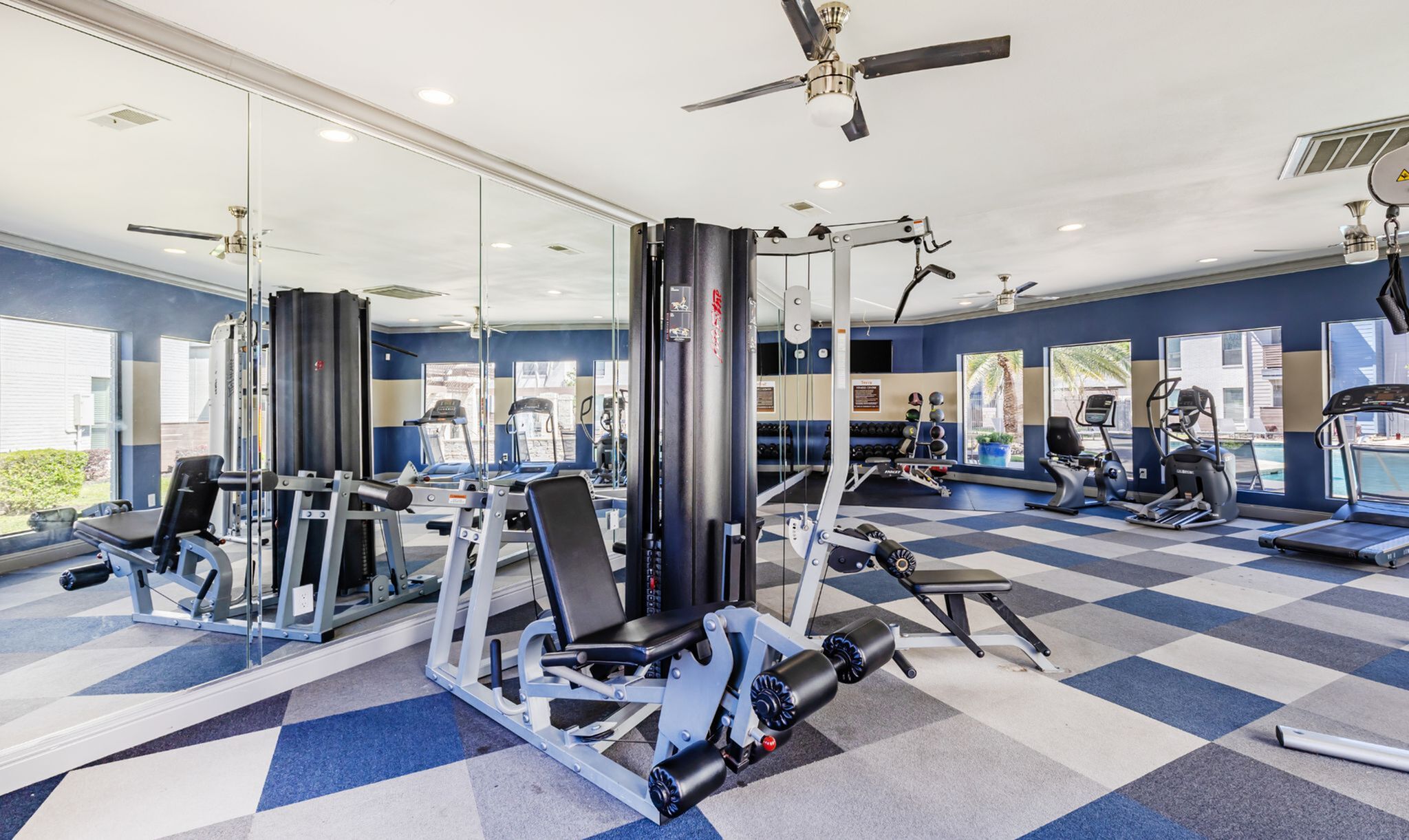 Modern fitness center with state-of-the-art gym equipment, mirrored walls, and large windows offering a bright and airy atmosphere.