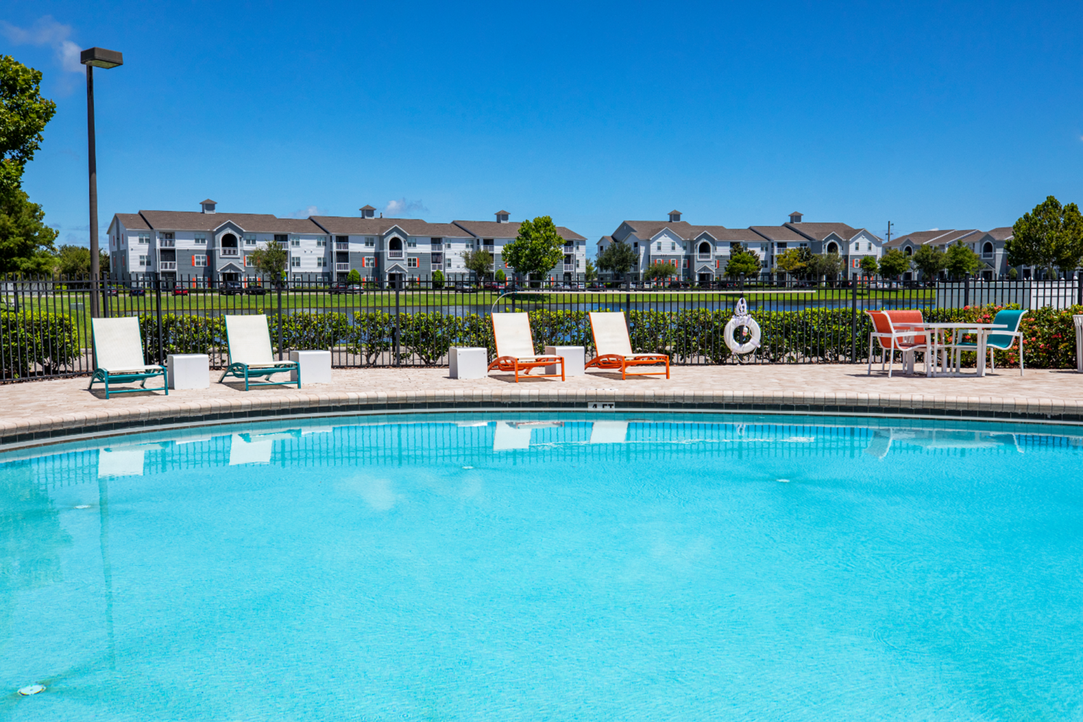 Inviting poolside view with comfortable lounge chairs, vibrant sun-kissed surroundings, and modern apartment buildings in the background.