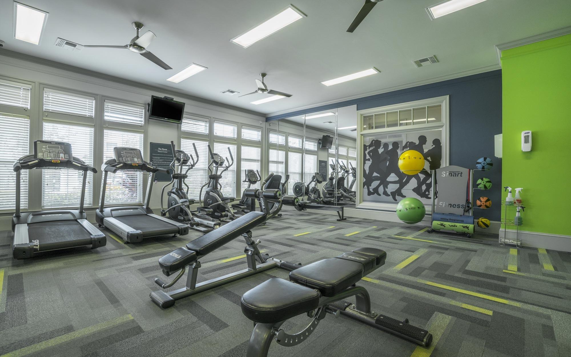 Modern fitness center with treadmills, elliptical machines, and workout benches, featuring vibrant green and blue accents.