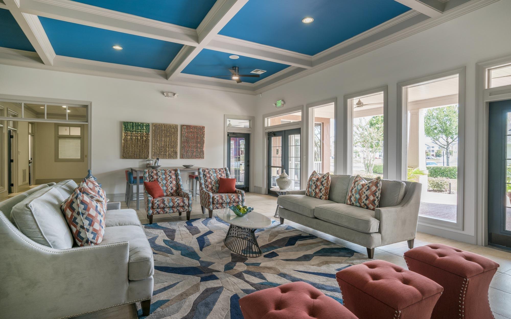 Elegant living room with modern design featuring a stylish blue coffered ceiling, plush sofas, and vibrant patterned accents. Bright natural light filters through large windows, creating an inviting and airy atmosphere.