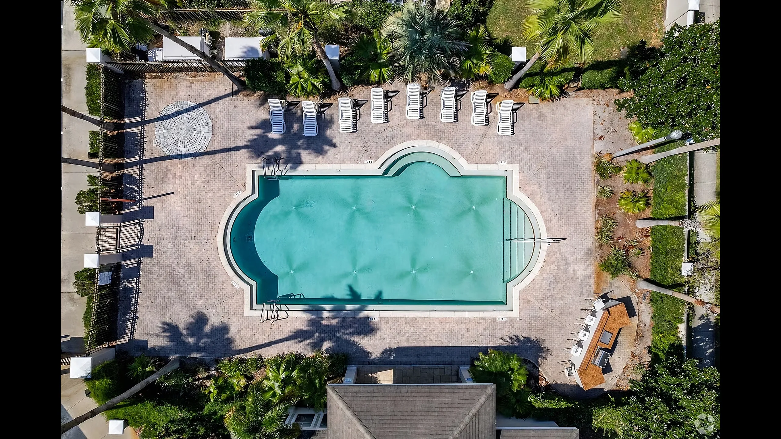 Aerial view of a luxurious outdoor swimming pool with elegant curves, surrounded by lush greenery and stylish lounge chairs, perfect for relaxation and entertainment.