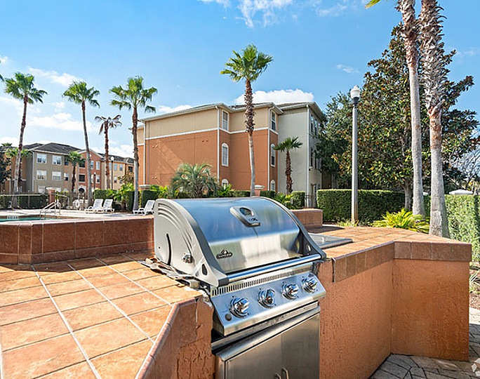 Charming outdoor grill area with sleek barbecue set against a backdrop of modern apartments and lush palm trees.