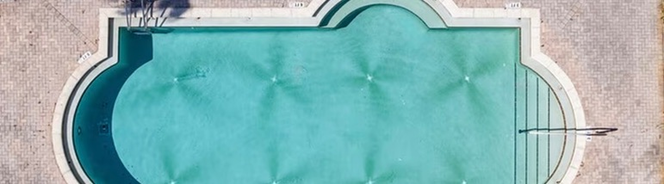 Elegant aerial view of a luxurious swimming pool surrounded by lush greenery and sun loungers, perfect for relaxation and leisure.