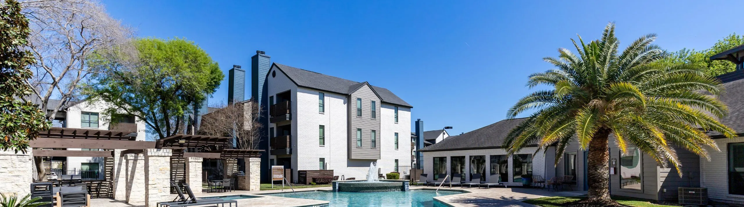 Elegant apartment complex with a resort-style pool, lush palm trees, and stylish outdoor seating, offering a luxurious living experience.