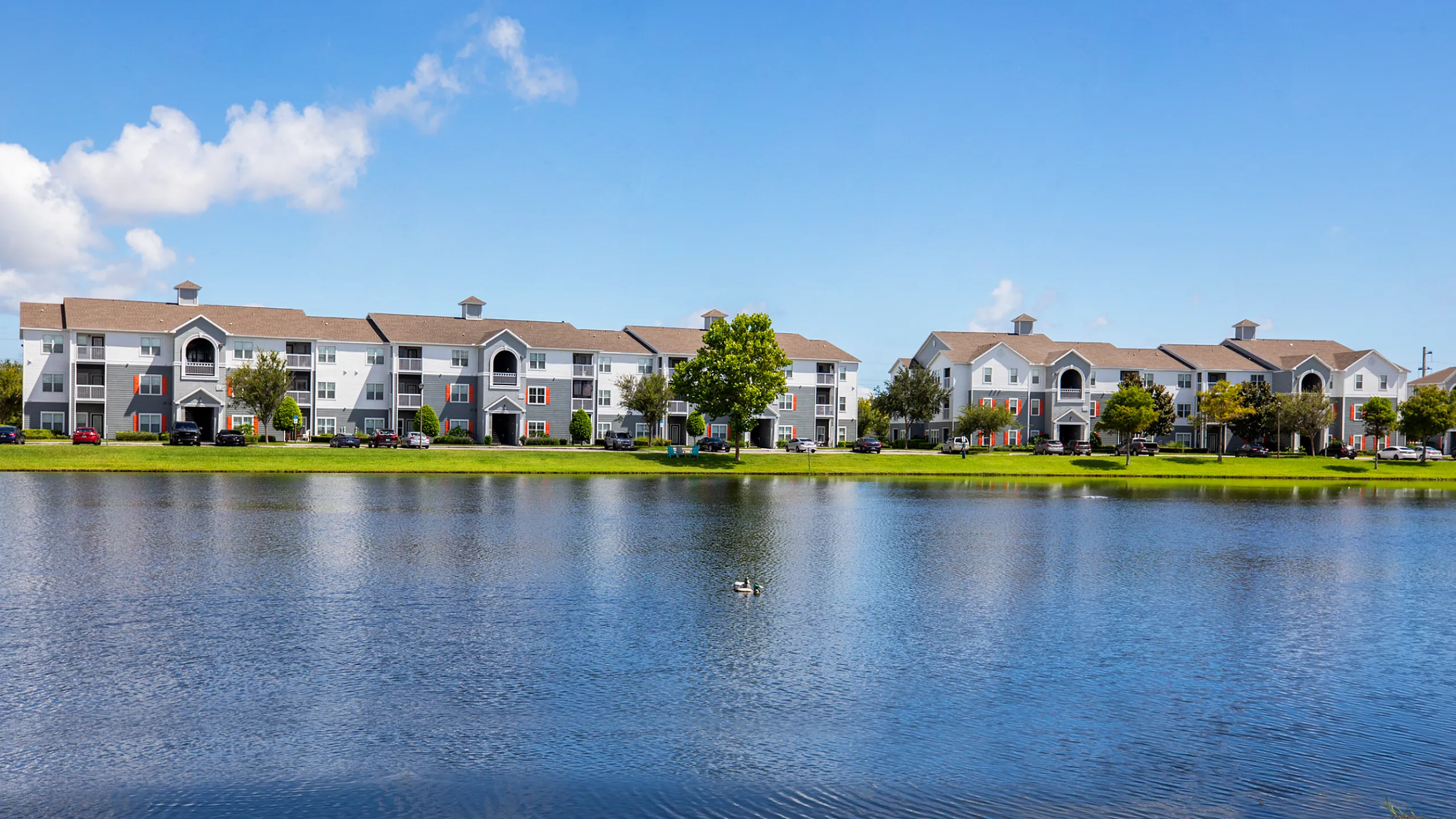 Inviting lakeside apartment complex with charming white buildings and lush greenery, perfect for serene living.
