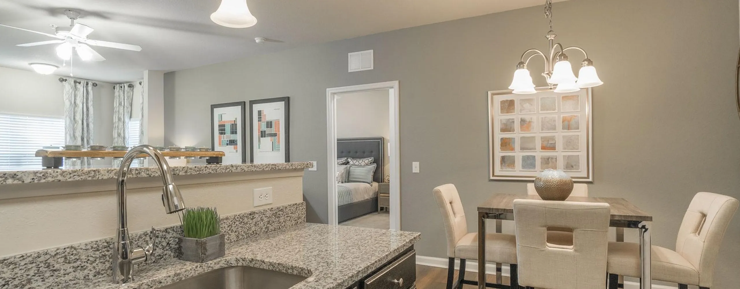 Elegant kitchen and dining area with sleek granite countertops, modern pendant lighting, and cozy seating for four, showcasing an inviting open layout with a glimpse of a stylish bedroom.