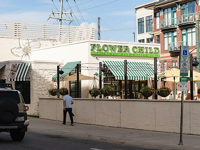 Charming urban restaurant exterior with green-striped awnings and hanging plants, offering a welcoming and fresh dining atmosphere.