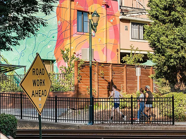 Vibrant urban view with a colorful mural on a modern building, surrounded by greenery and active pedestrians.