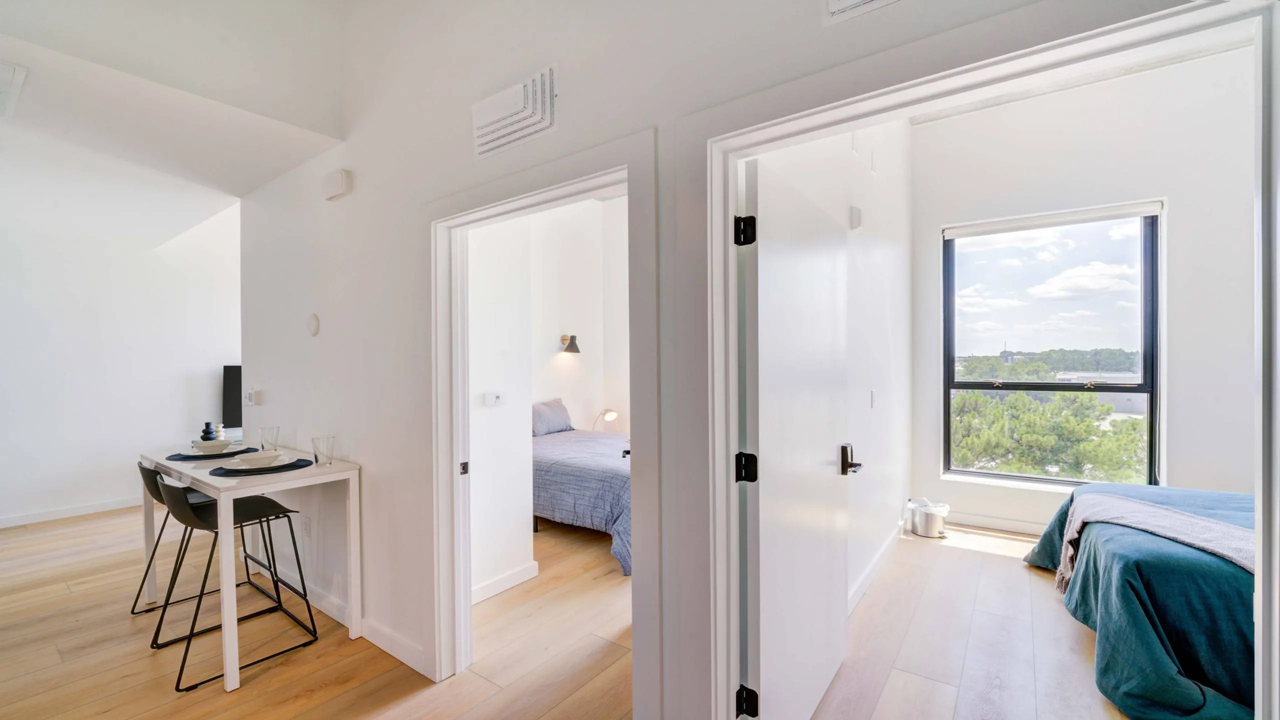 Bright, modern apartment showcasing two cozy bedrooms with large windows and a sleek dining area, perfect for urban living.