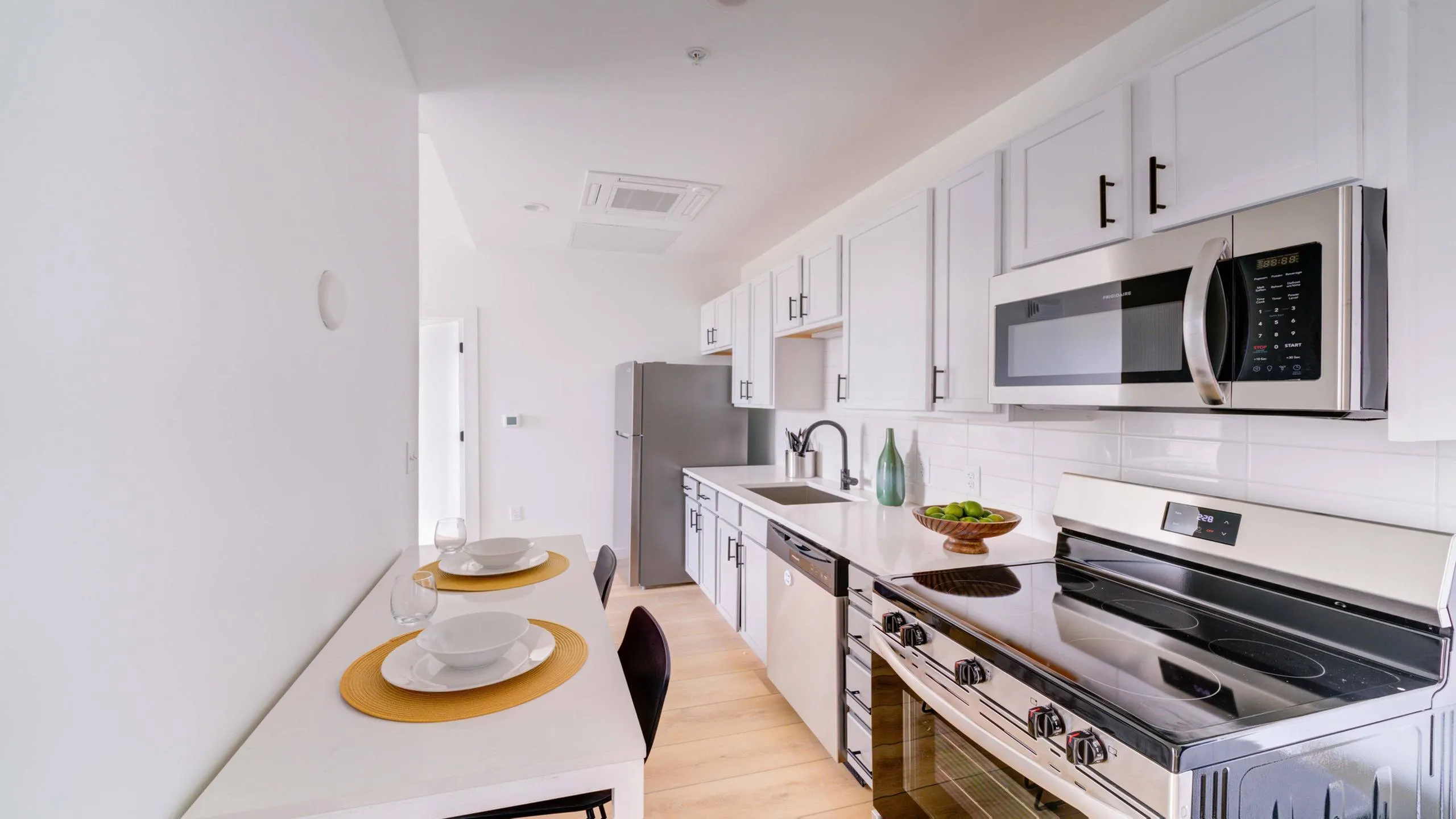 Modern kitchen with sleek stainless steel appliances, quartz countertops, and elegant white cabinetry. Cozy dining area with stylish place settings and bright natural light.