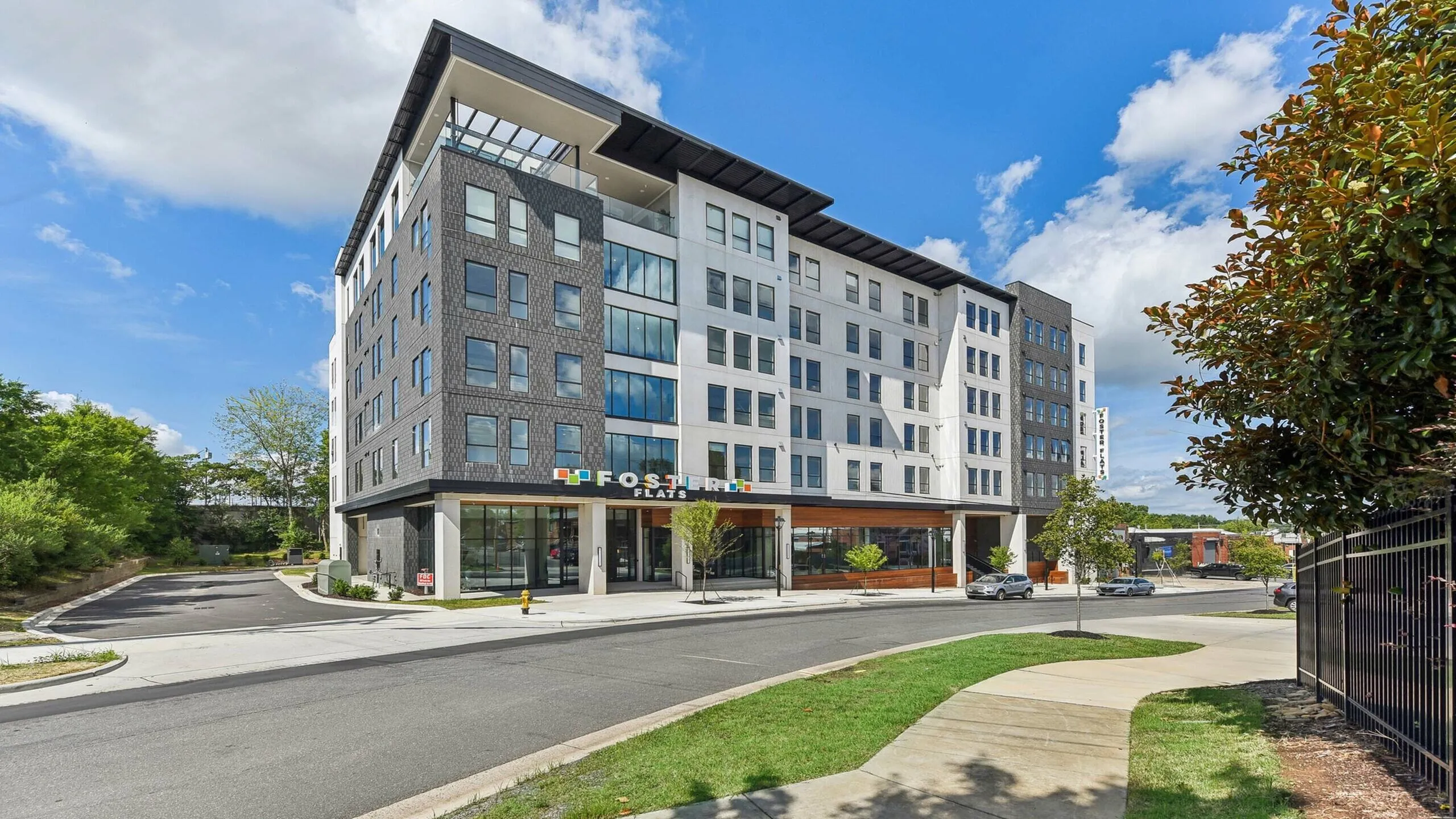 Modern urban apartment complex showcasing sleek architecture with large windows and a stylish facade, surrounded by lush greenery under a bright blue sky.