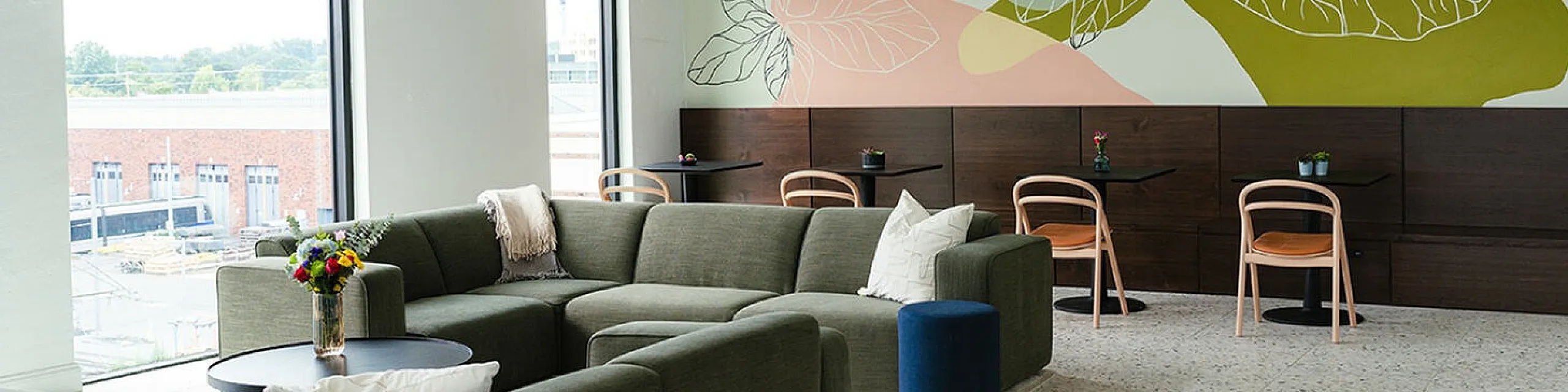 Bright, modern lounge area with large windows, vibrant wall art, cozy sectional sofa, and stylish dining setup.