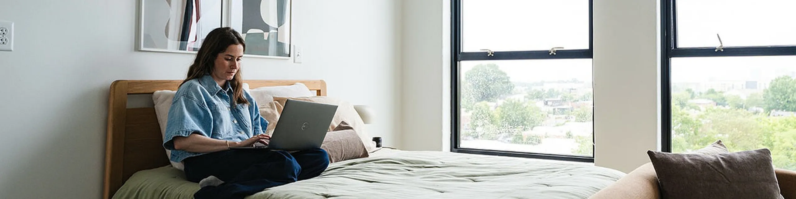 Bright, modern bedroom with large windows, featuring cozy decor, chic artwork, and a relaxed atmosphere perfect for working from home.