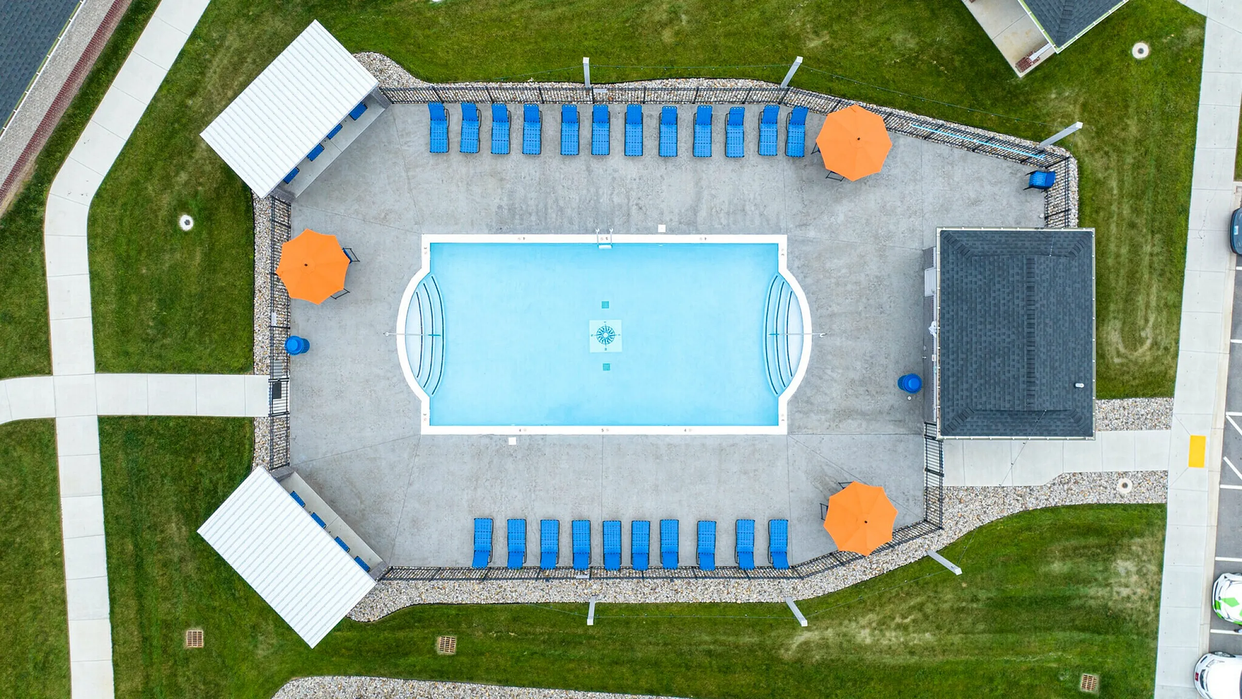 Aerial view of a luxurious swimming pool area surrounded by blue lounge chairs and bright orange umbrellas, creating a vibrant and inviting outdoor recreation space.