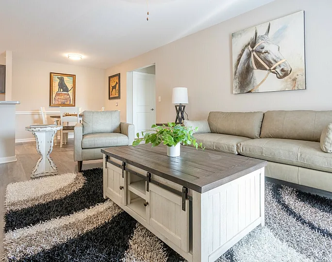 Inviting living room with plush beige sofas, a rustic wooden coffee table, and stylish horse artwork, offering a cozy and sophisticated atmosphere.