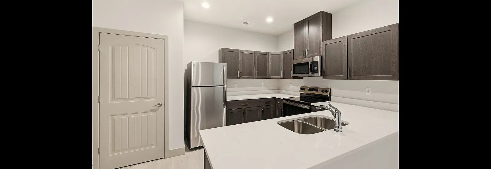 Modern kitchen with sleek stainless steel appliances, elegant dark wood cabinetry, and a spacious marble countertop with a double sink.