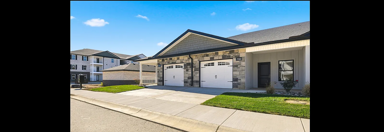 Charming suburban apartment building featuring modern stonework, lush green lawns, and a clean, inviting driveway.