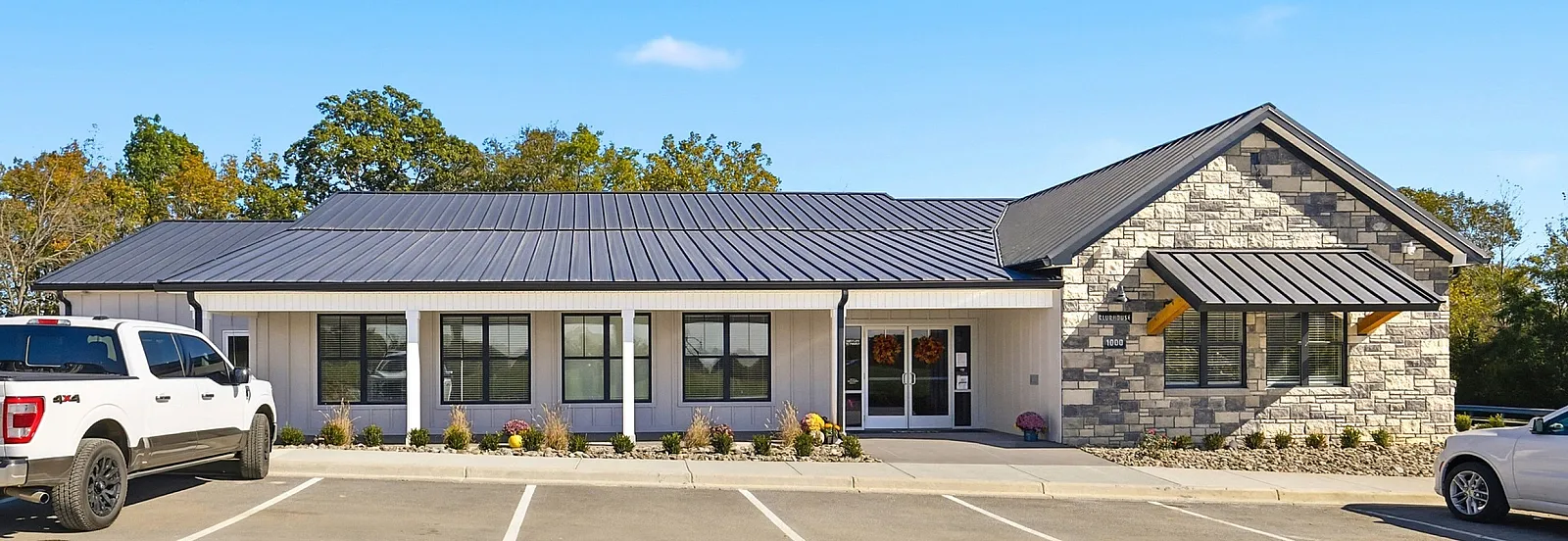 Charming modern building with a sleek metal roof, surrounded by a well-maintained parking area and lush greenery under a clear blue sky.