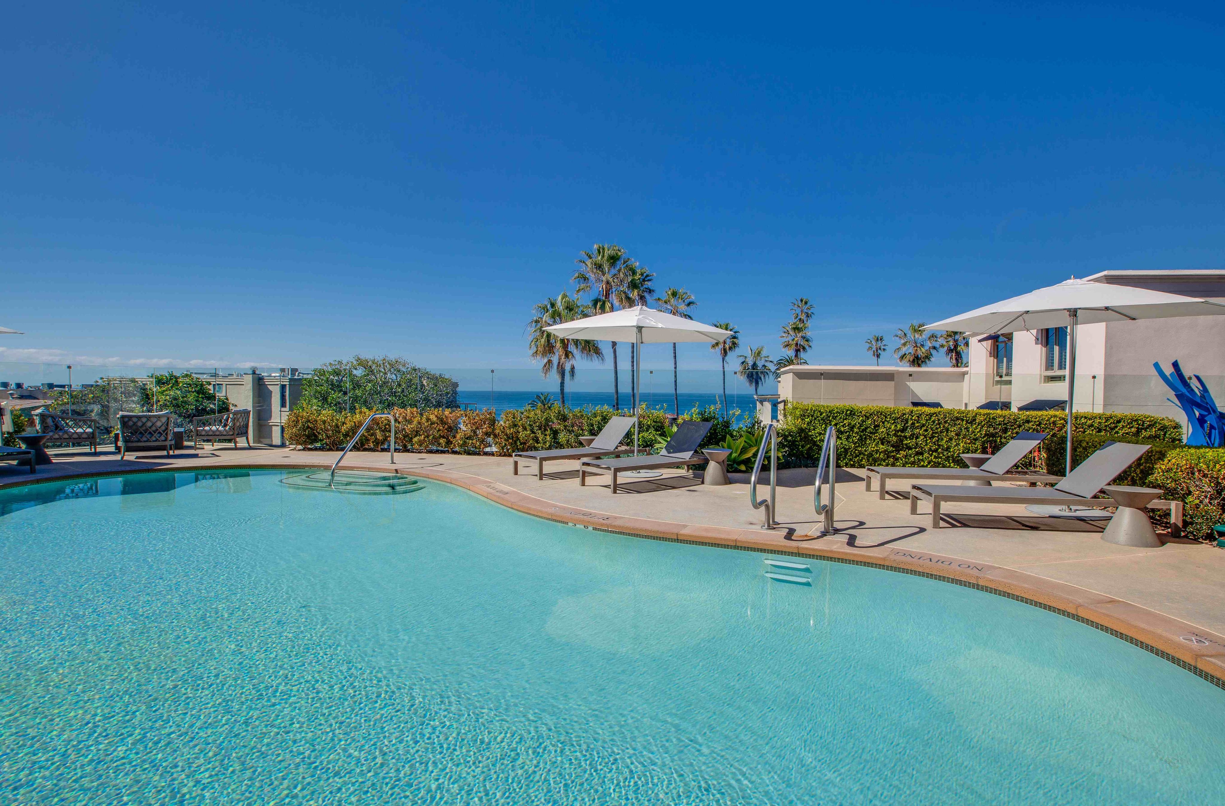 Luxurious poolside retreat with ocean views, surrounded by palm trees and elegant lounge chairs, featuring vibrant blue skies.