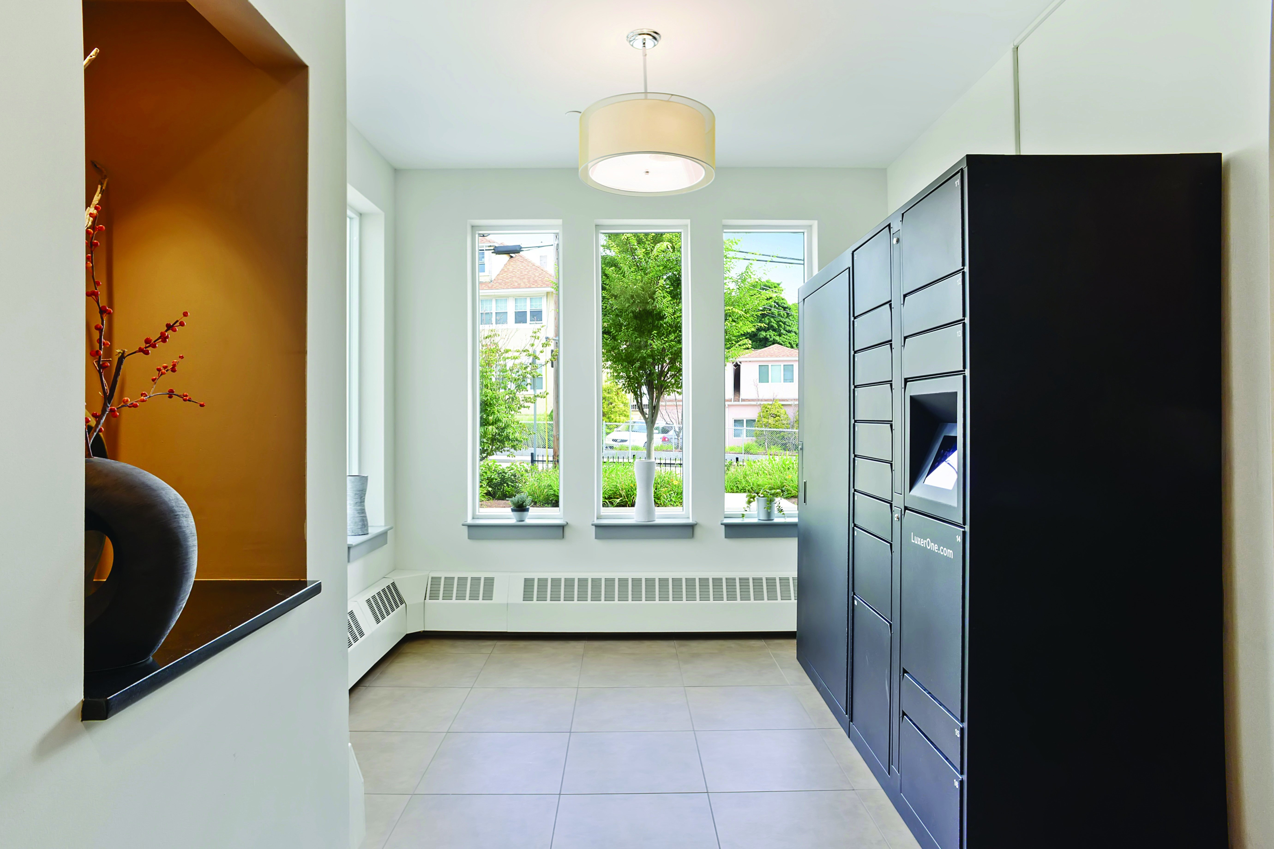 Contemporary apartment lobby with sleek black package lockers, large windows offering natural light, and stylish decor accents.