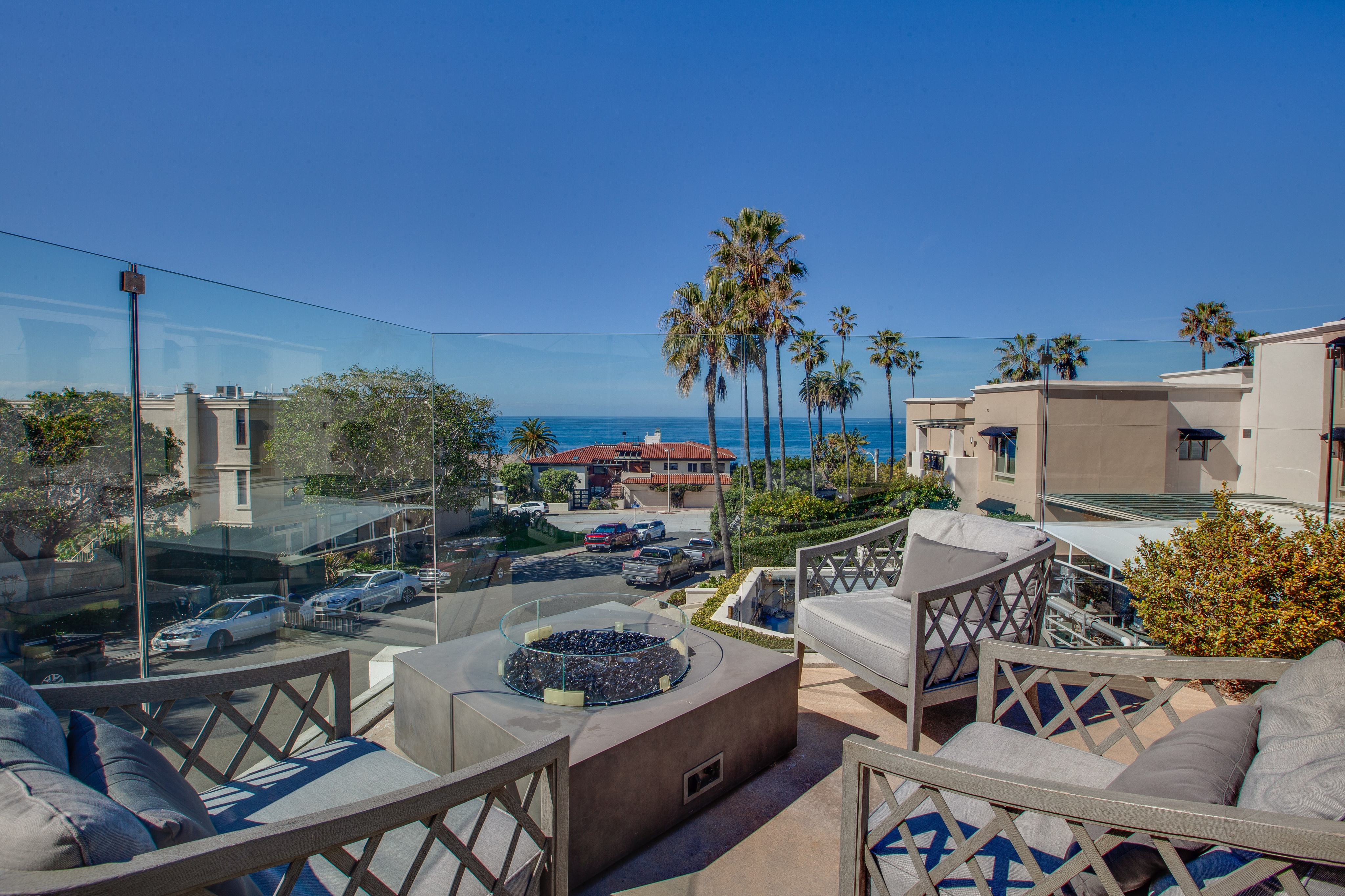 Luxurious terrace overlooking a stunning ocean view with palm trees and a stylish outdoor seating area around an outdoor fireplace.