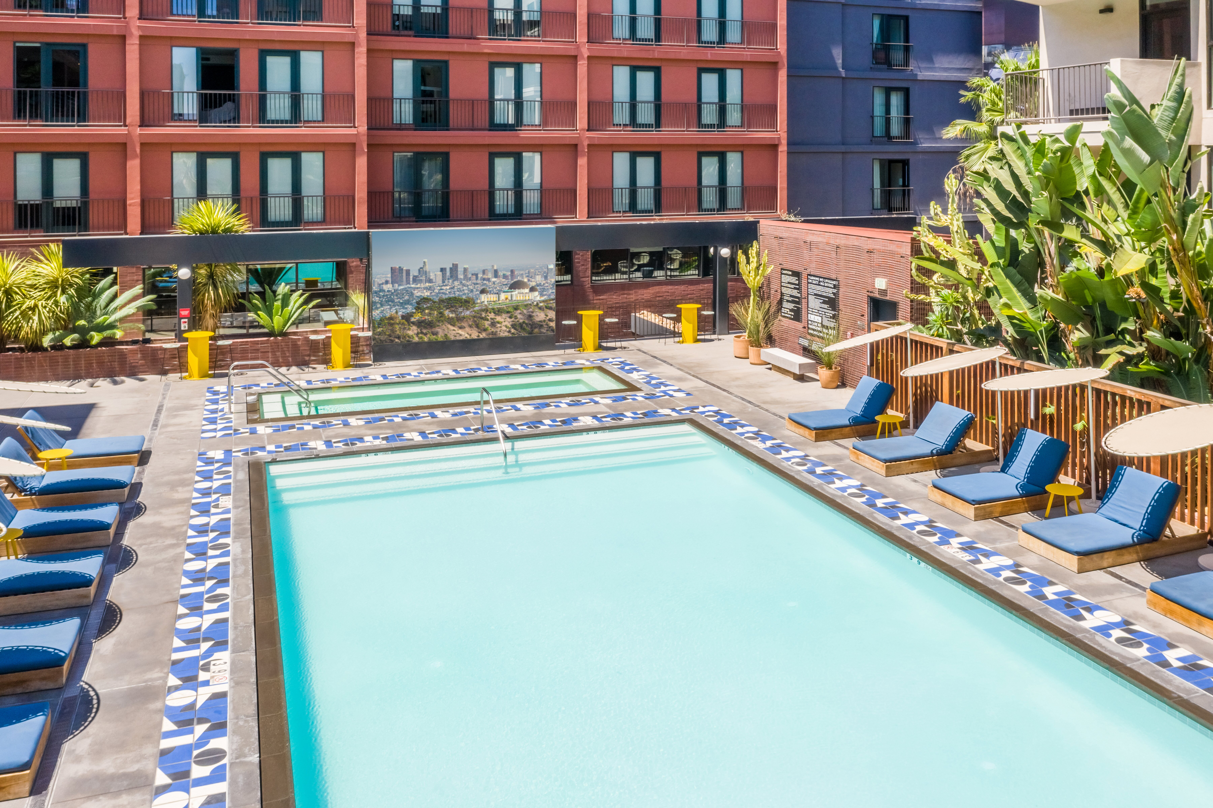 Vibrant apartment complex with a refreshing outdoor pool, stylish lounge chairs, and lush greenery, offering a perfect relaxation spot in a modern urban setting.
