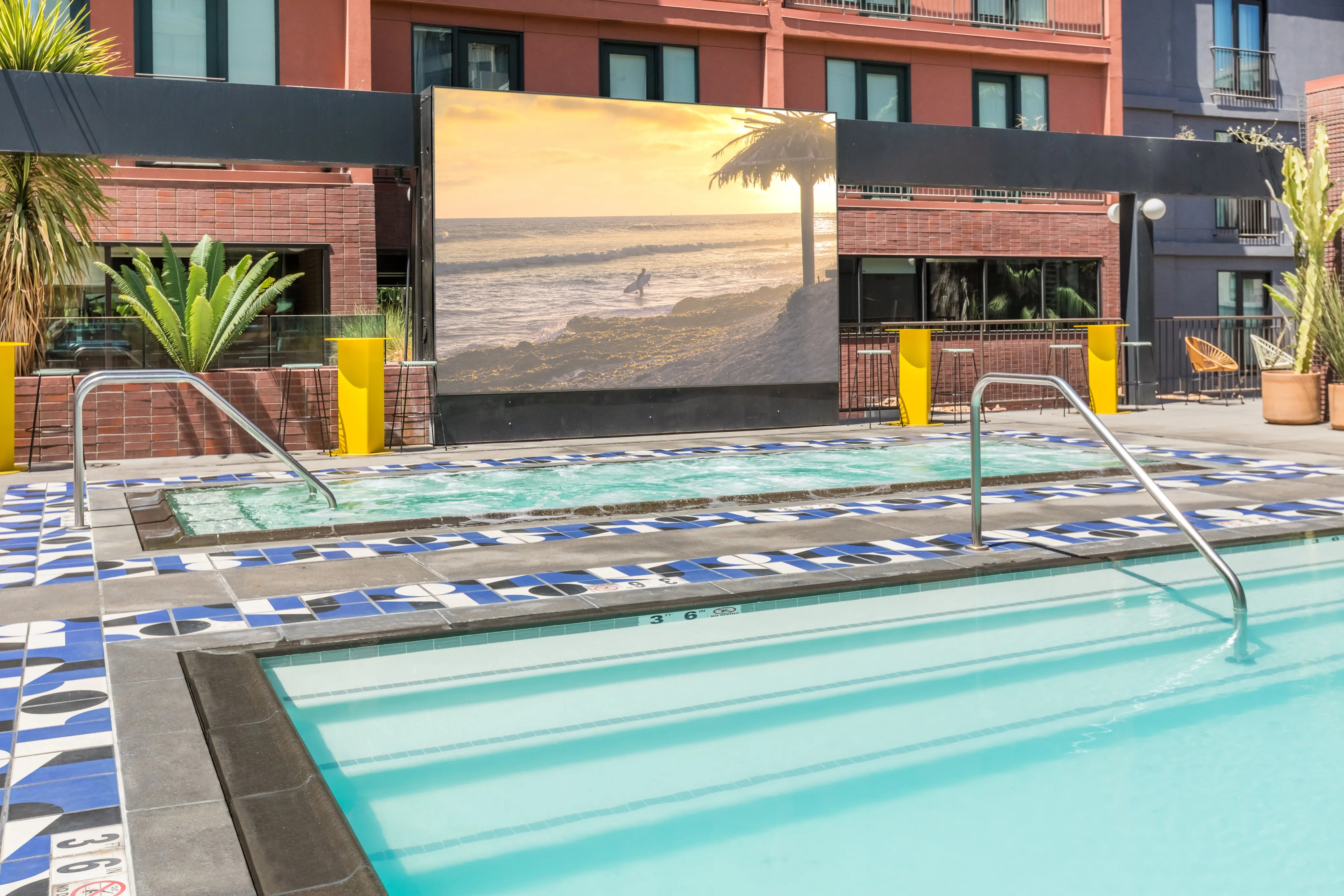 Chic apartment complex with a modern outdoor pool area, vibrant blue and white tile accents, lush plants, and a serene beach mural.