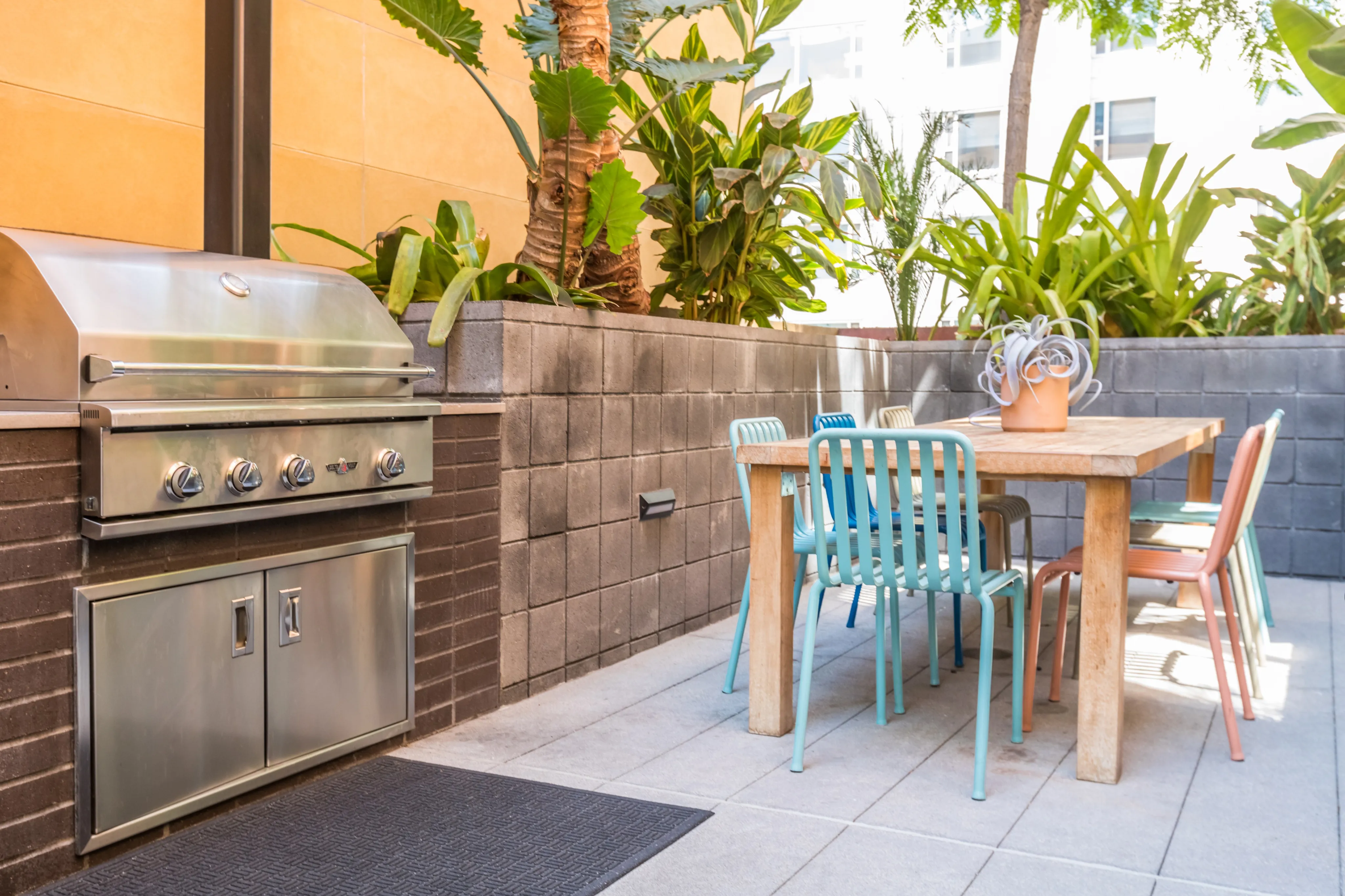Chic outdoor patio featuring a stainless steel grill and colorful dining set surrounded by lush greenery.