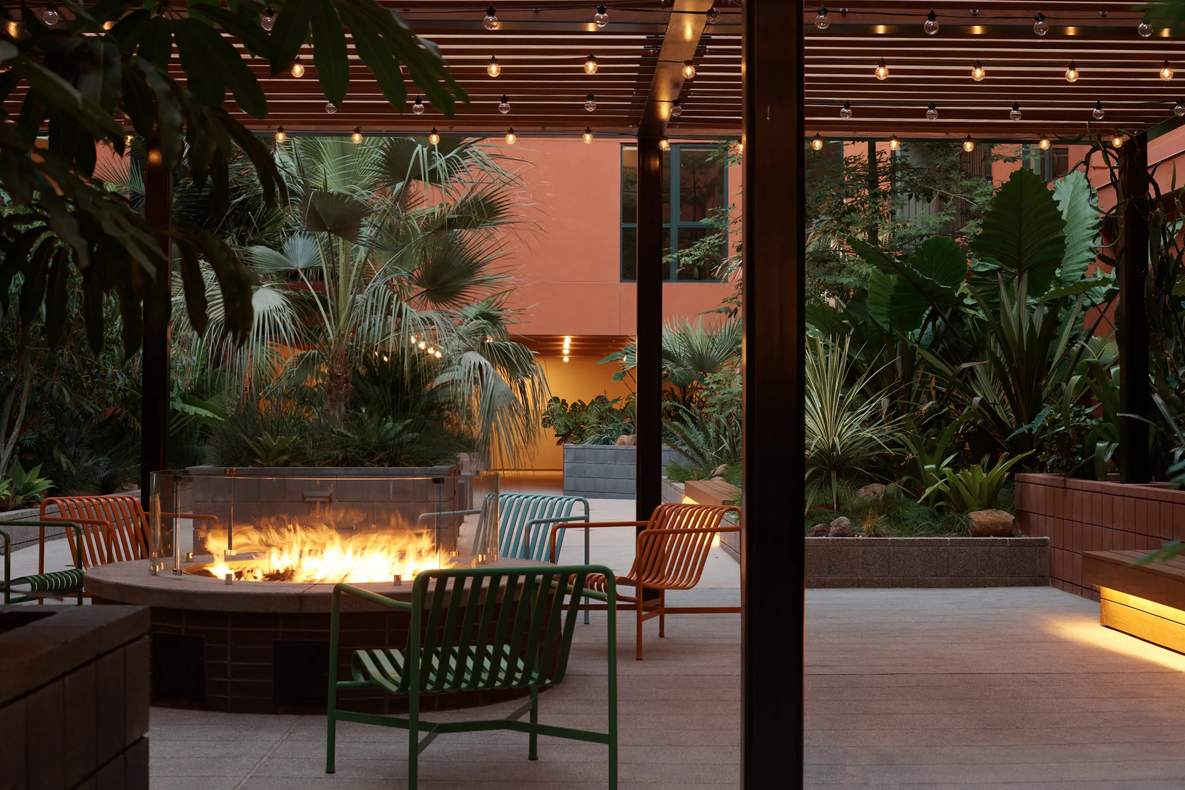 Chic outdoor patio with modern lighting, lush greenery, and a cozy fire pit surrounded by colorful seating.