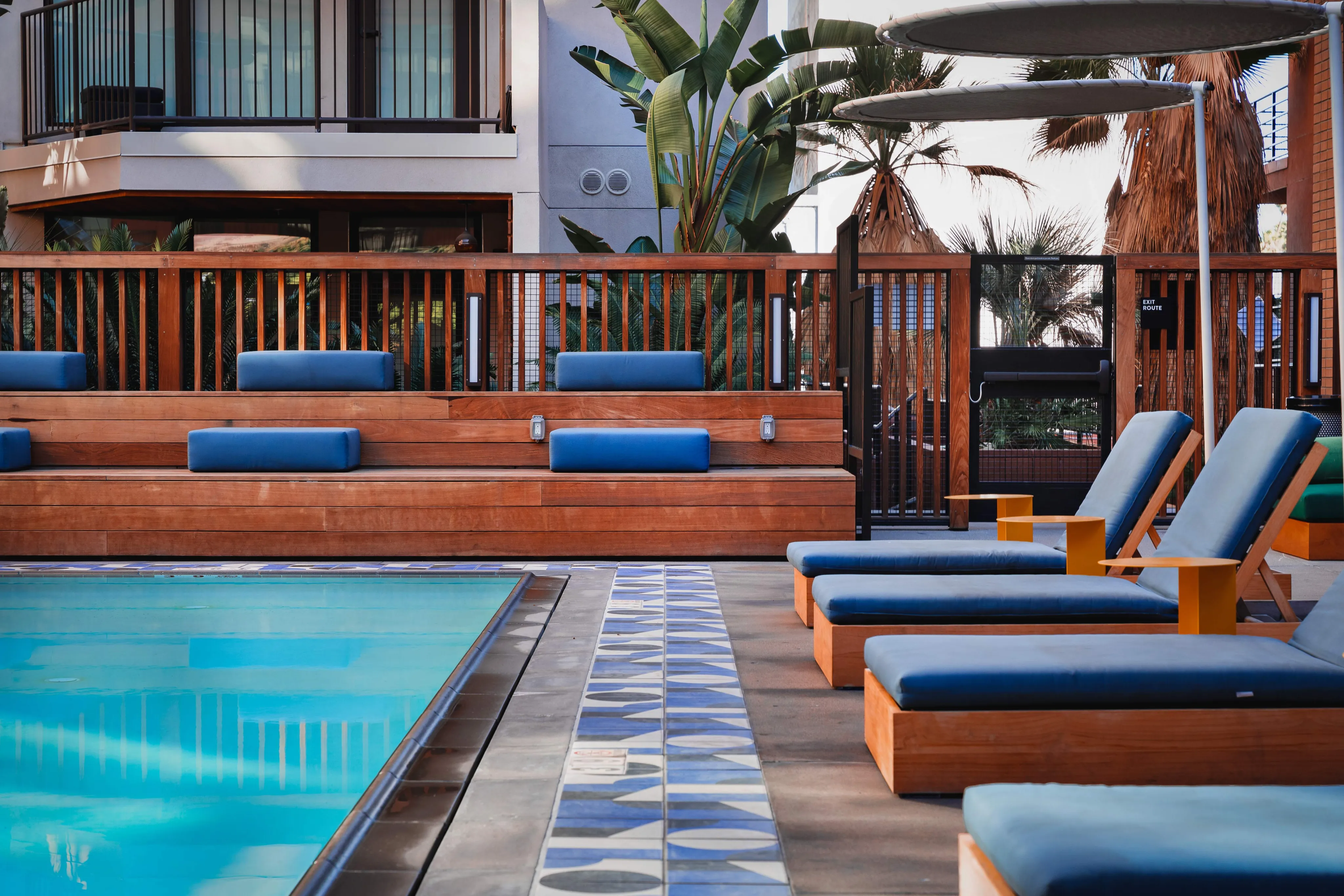Luxurious poolside with modern lounge chairs and stylish wooden deck amid lush tropical plants.
