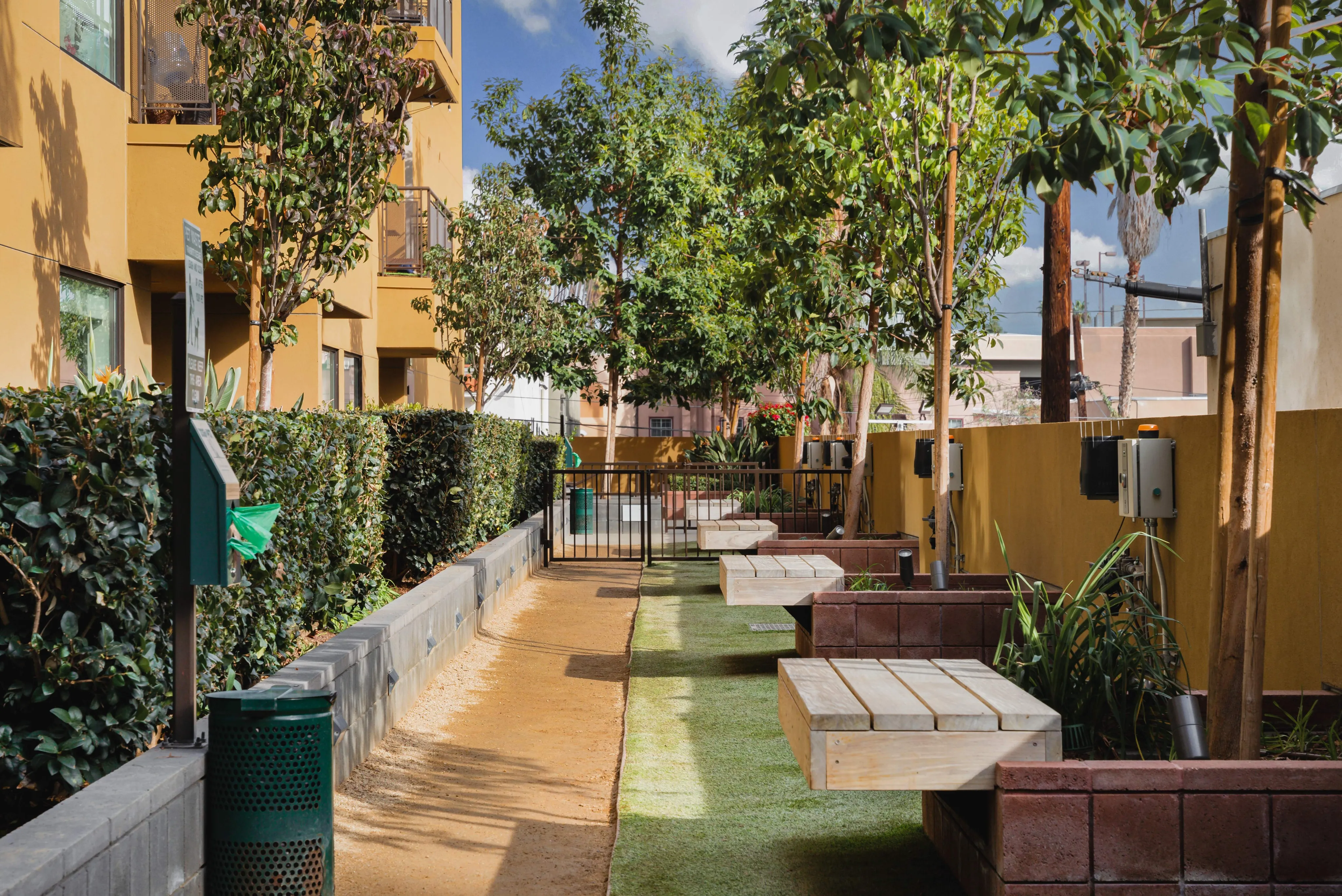Tranquil apartment courtyard with lush greenery, modern benches, and path under a clear sky.