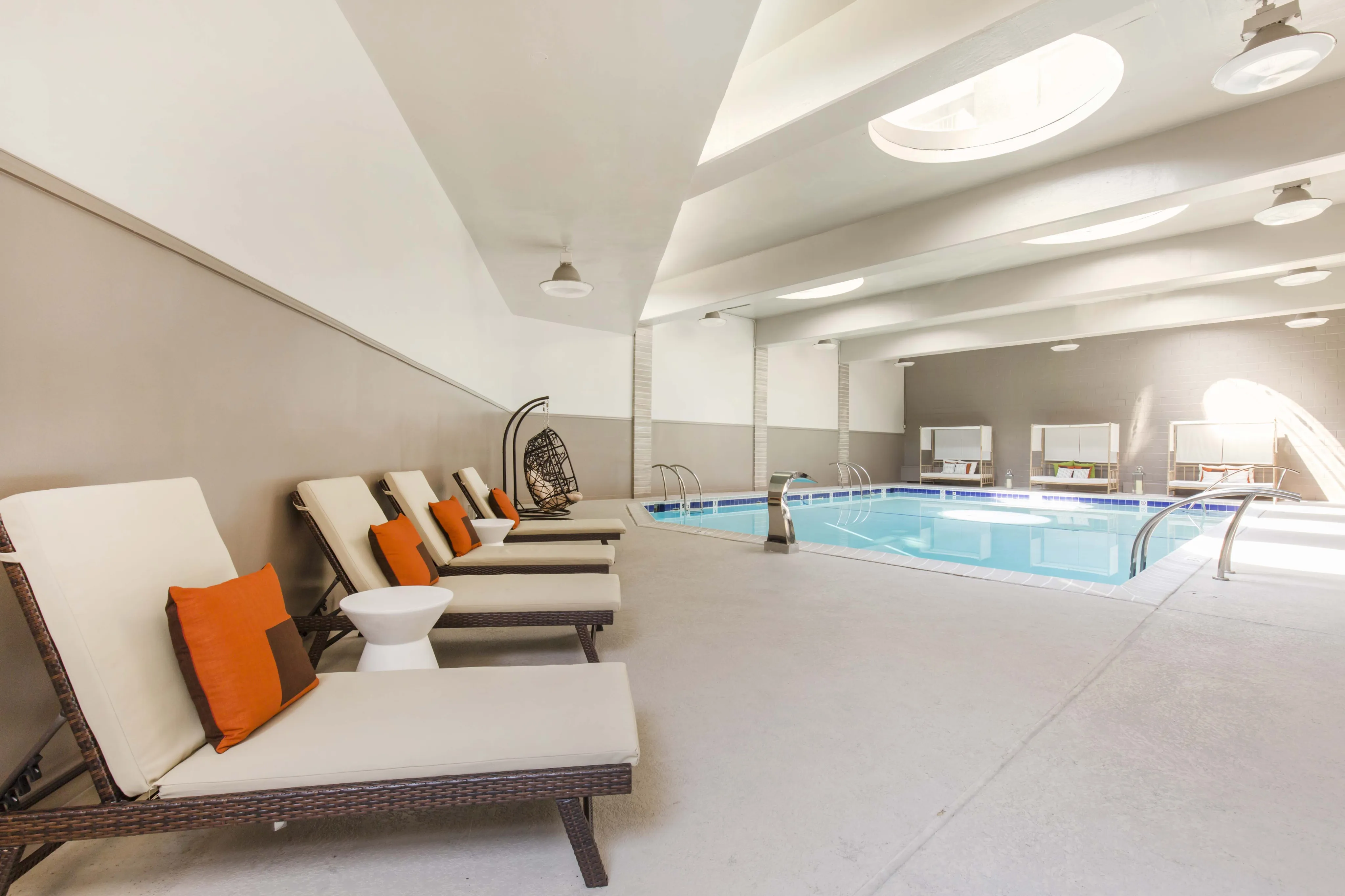 Elegant indoor pool area with stylish lounge chairs and vibrant orange cushions, perfect for relaxation and leisure.