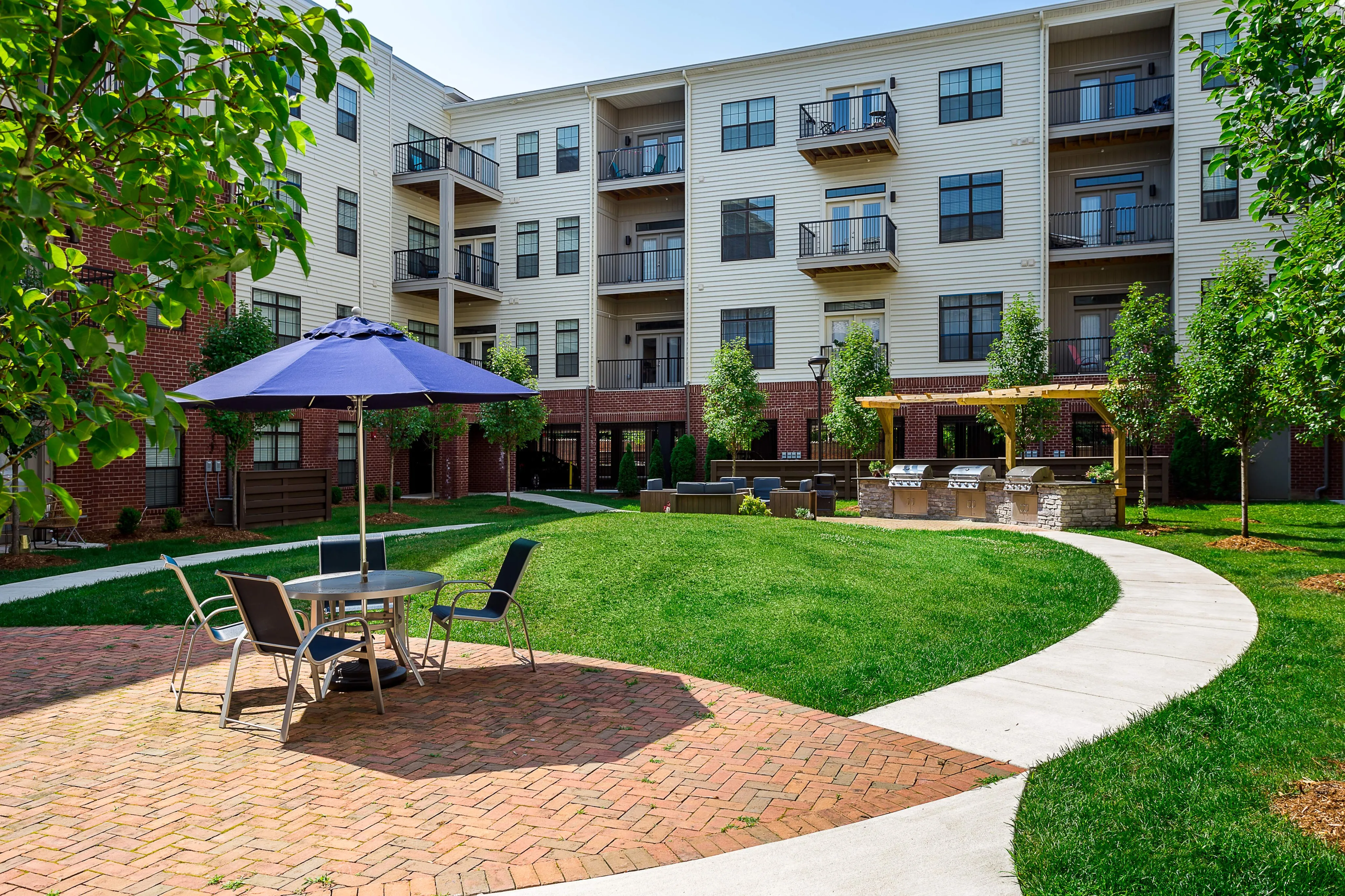 Inviting apartment courtyard featuring stylish outdoor seating, a vibrant green lawn, and a modern barbecue area under a pergola.
