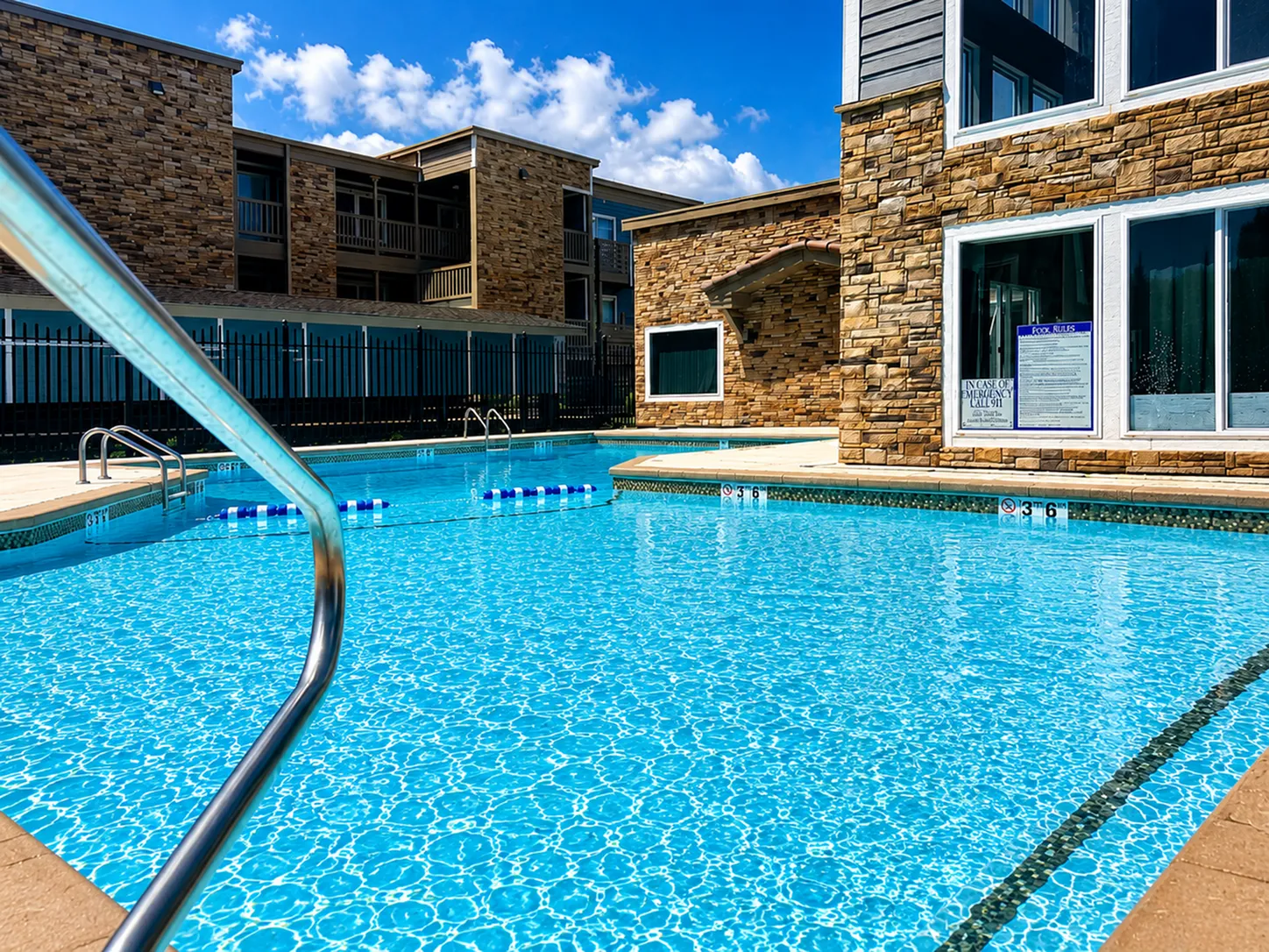 Inviting outdoor pool area with sparkling blue water surrounded by modern stone architecture and sunny skies.