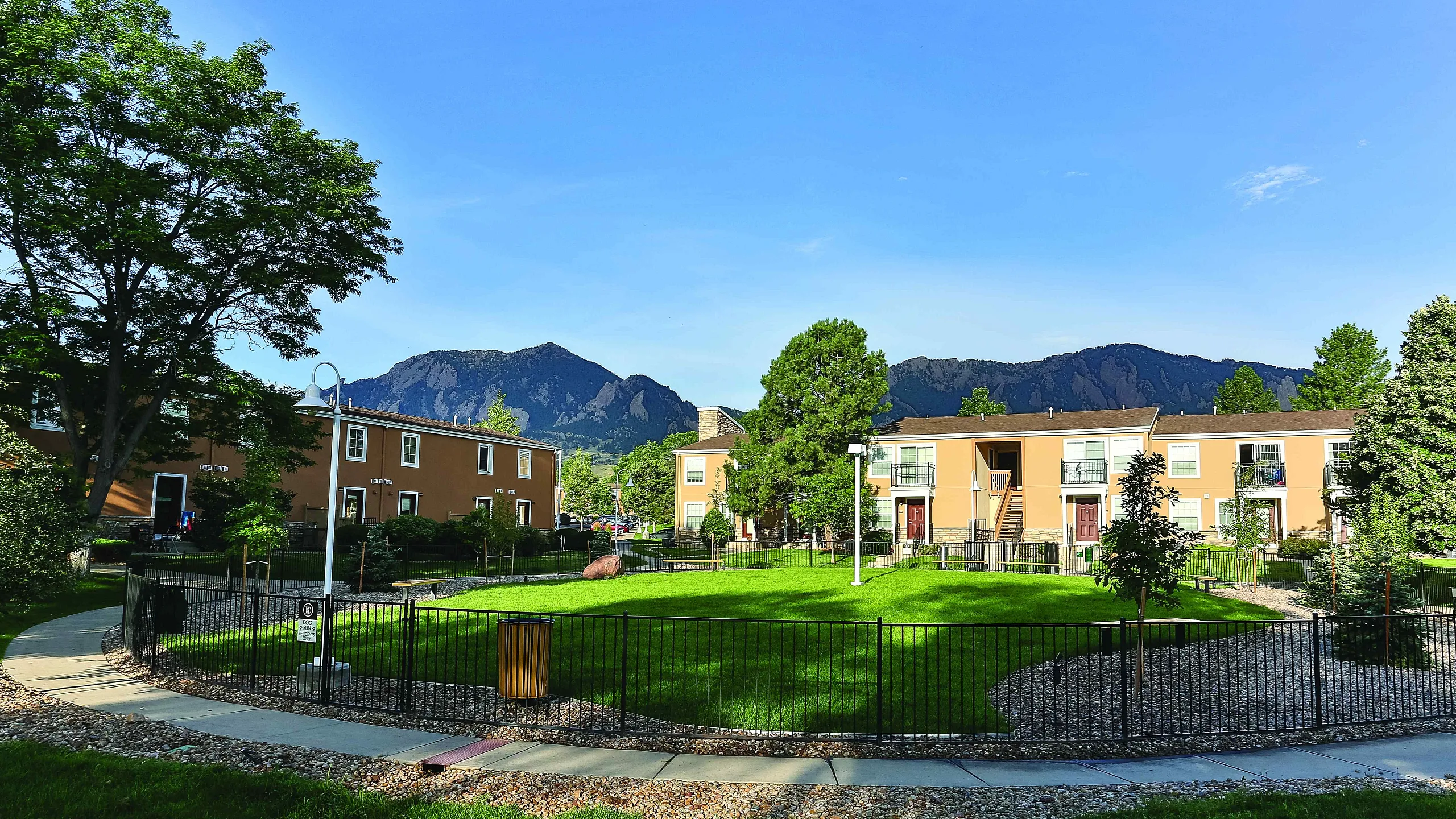 Charming apartment complex with a lush green courtyard and striking mountain views under a clear blue sky.