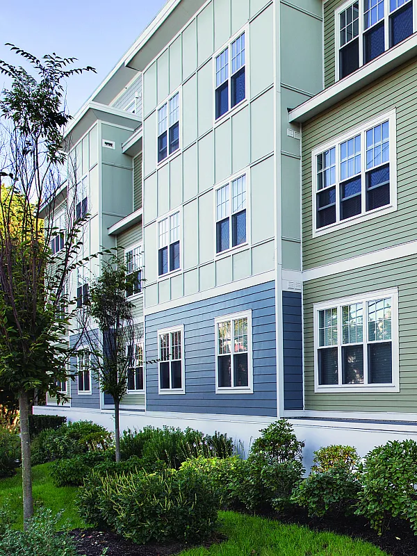 Charming modern apartment exterior with colorful siding and lush landscaping, featuring elegant windows.