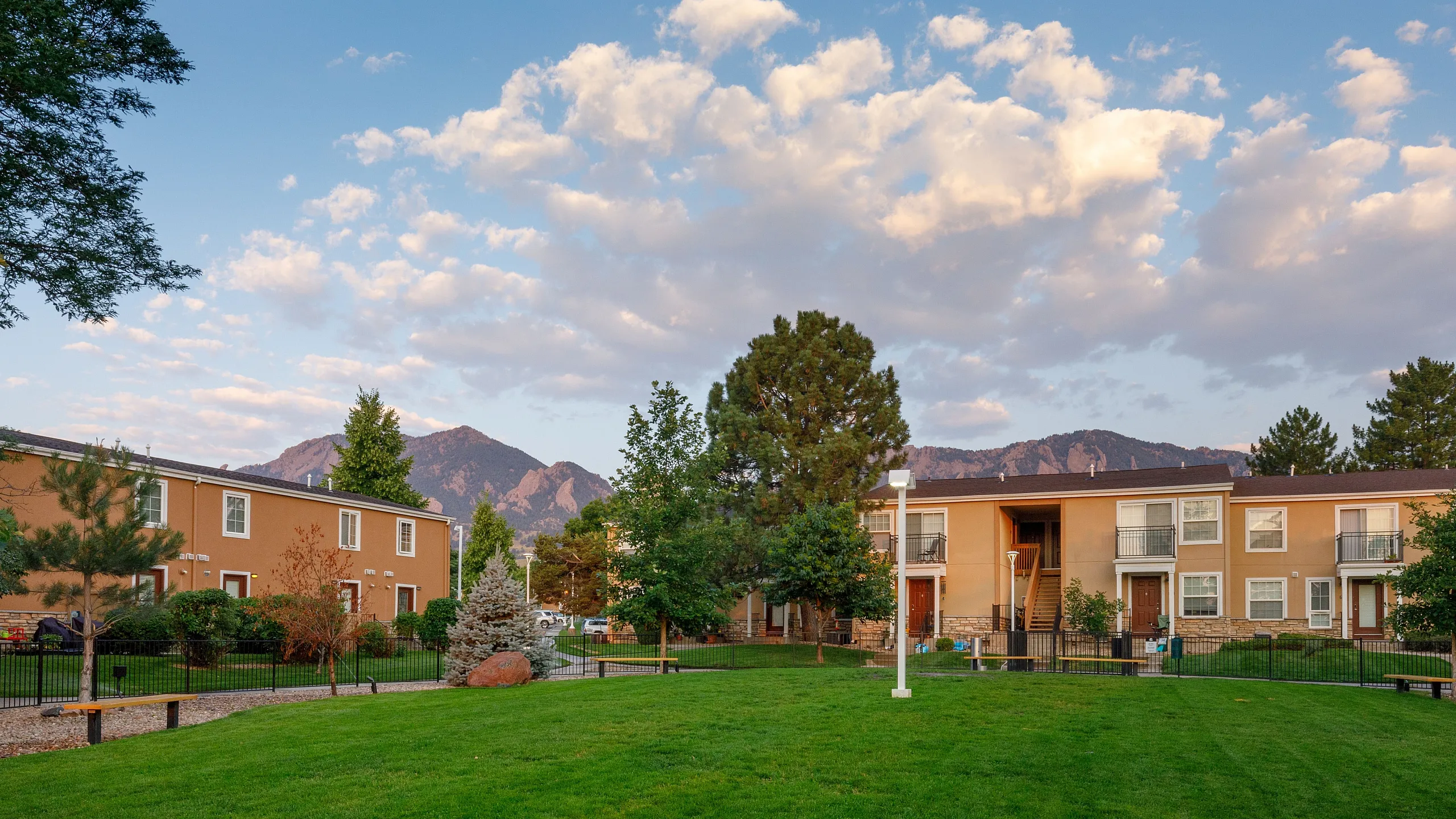 Charming apartment complex surrounded by lush greenery and framed by stunning mountain views under a vibrant blue sky.