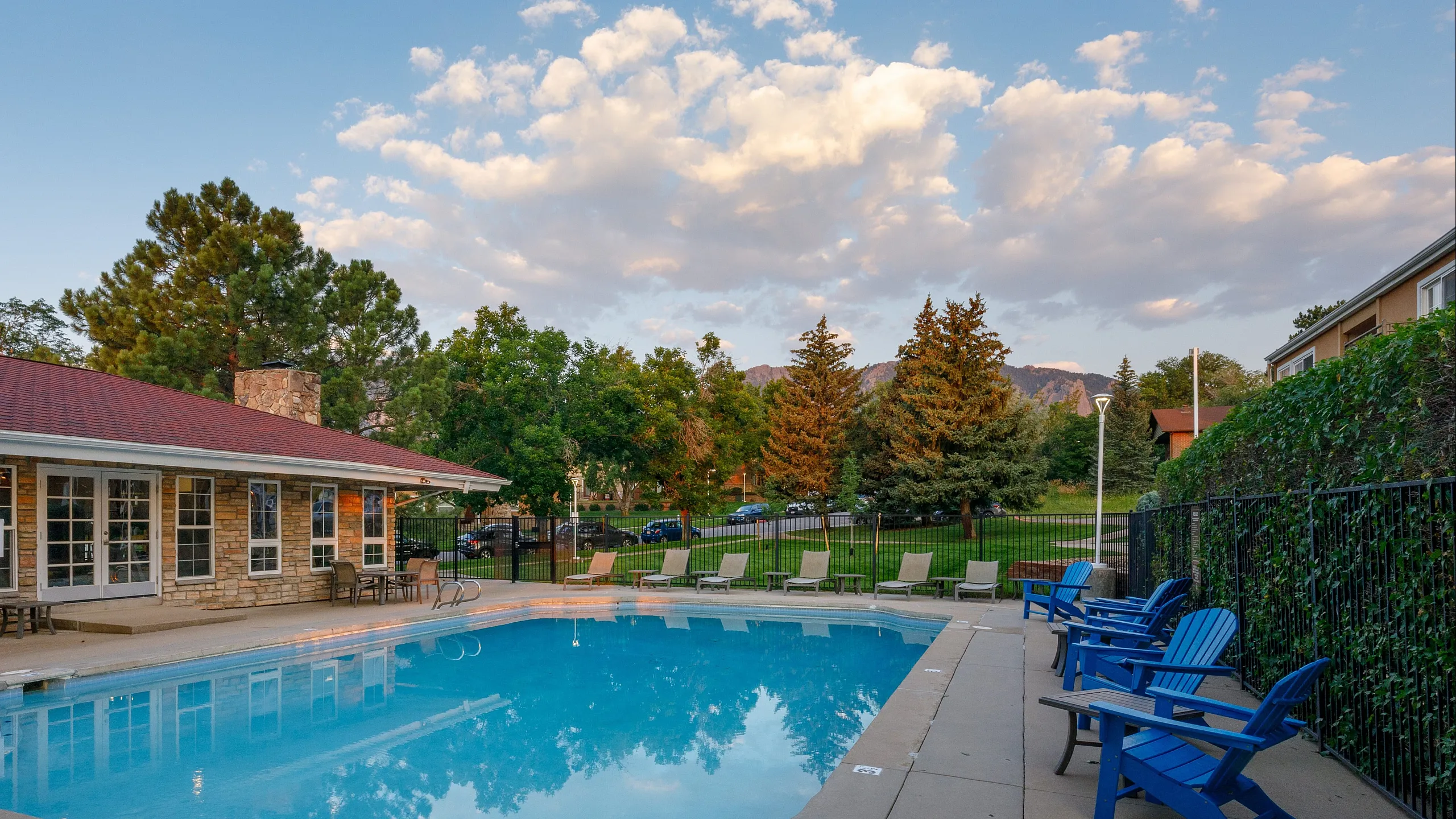 Charming outdoor pool area with lush greenery and mountain views, featuring cozy blue Adirondack chairs and inviting lounge spaces.