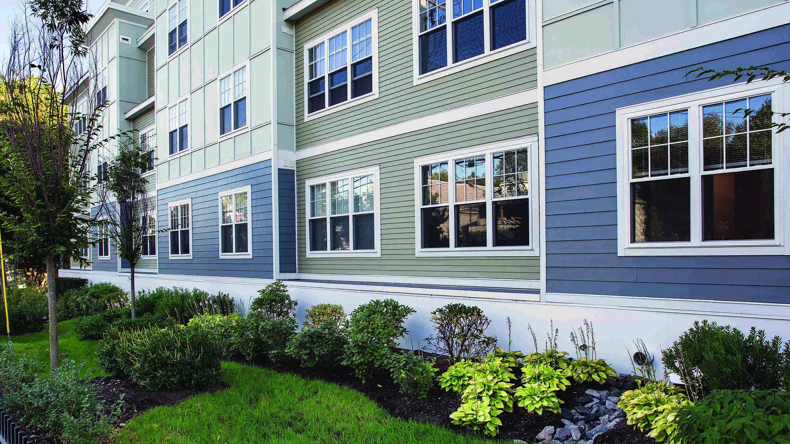 Charming apartment building with modern siding and large windows, surrounded by lush greenery and well-maintained landscape.